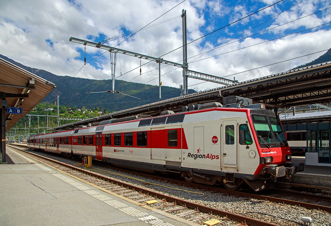 Der dreiteilige NPZ Domino RA12 der RegionAlps (ex SBB RBDe 4/4) hat am 25.05.2023 als Regio (St-Gingolph–St-Maurice –Martigny–Sion–Brig), Steuerwagen voraus, seinen Zielbahnhof Brig erreicht.

Der NPZ Domino besteht aus:
1./2. Klasse Steuerwagen ABt NPZ DO RA 50 85 39-43 948-1 CH-RA
Modernen 2.Klasse INOVA-Zwischenwagen mit Niederfluranteil B NPZ DO RA 50 85 29-43 407-0 CH-RA
und dem 
Triebwagen RBDe 560 DO RA 94 85 7 560 412-9 CH-RA, ex SBB RBDe 560 010-1 (Umbau 2009), hier rechts im Vordergrund.

Die Regionalps (RA) ist ein Eisenbahnverkehrsunternehmen im Kanton Wallis, mit Sitz in Martigny hat. Eigentümer derim Jahr 2003 gegründete Gesellschaft  sind die Schweizerischen Bundesbahnen (SBB) mit 70 %, die Transports de Martigny et Régions (TMR) mit 18 % und der Kanton Wallis mit 12 %. Die RA betreibt den Regionalverkehr vor allem im Rhonetal zwischen dem Ostufer des Genfersees und Brig. Inzwischen gehören Regionalps 16 dreiteilige NPZ Domino (Trieb-, Zwischen- und Steuerwagen ex SBB) und 4 RABe 525 NINA (ex TMR).

Als RBDe 4/4 wurden die Triebwagen der Schweizerischen Bundesbahnen (SBB) bezeichnet, die ab 1984 für die als Neuer Pendelzug (NPZ) bezeichneten Regionalzugskompositionen mit den dazugehörenden Steuerwagen angeschafft wurden. Sie tragen seit 1990 die Baureihenbezeichnung RBDe 560. Aus Kostengründen wurde damals auf die Beschaffung neuer Zwischenwagen verzichtet, verwendet werden stattdessen umgebaute Einheitswagen (EW I und EW II).

Die meisten von 1987 bis 1996 gebauten Fahrzeuge RBDe 560, 561 und 568 durchliefen 2008 bis 2013 ein Komplett-Modernisierungsprogramm. Aus aufgearbeiteten Trieb- und Steuerwagen sowie neu beschafften Zwischenwagen entstanden Regionalverkehrs-Kompositionen mit der Bezeichnung «Domino». Die Triebwagen werden dabei einheitlich als RBDe 560 (94 85 7 560 XXX-X) bezeichnet. Sie können in Vielfachsteuerung verkehren.

TECHNISCHE DATEN (Komposition RBDe 560, B und ABt) :
Spurweite:  1.435 mm (Normalspur)
Achsformel:  Bo’Bo’ +2´2´+2´2´
Länge über Puffer:  25.000 mm / 24.700 mm / 25.000 mm
Drehzapfenabstand: 17.600 mm / 18.900 mm /17.600 mm
Achsabstand im Drehgestell: 2.700 mm (ZW 2.500 mm)
Treib- und Laufraddurchmesser: 950 mm
Höhe:  3.750 mm
Breite:  2.860 mm
Dienstgewicht:  72 t (Triebwagen) + 36 t (ZW) + 38 t (Steuerwagen)
Höchstgeschwindigkeit: 140 km/h
Dauerleistung:  1.650 kW (2.250 PS)
Anfahrzugkraft:  182 kN
Dauerzugkraft: 78 kN
Anzahl Fahrmotoren: 4
Stromsystem:  Wechselstrom 15 kV 16,7 Hz
Sitzplätze: 54 (TW) / 60 (ZW) / 12+60 (SW) = 186 (12 in der 1. Klasse)
Ladegewicht: 0,3 t (Triebwagen)
Kupplungstyp: Schraubenkupplung