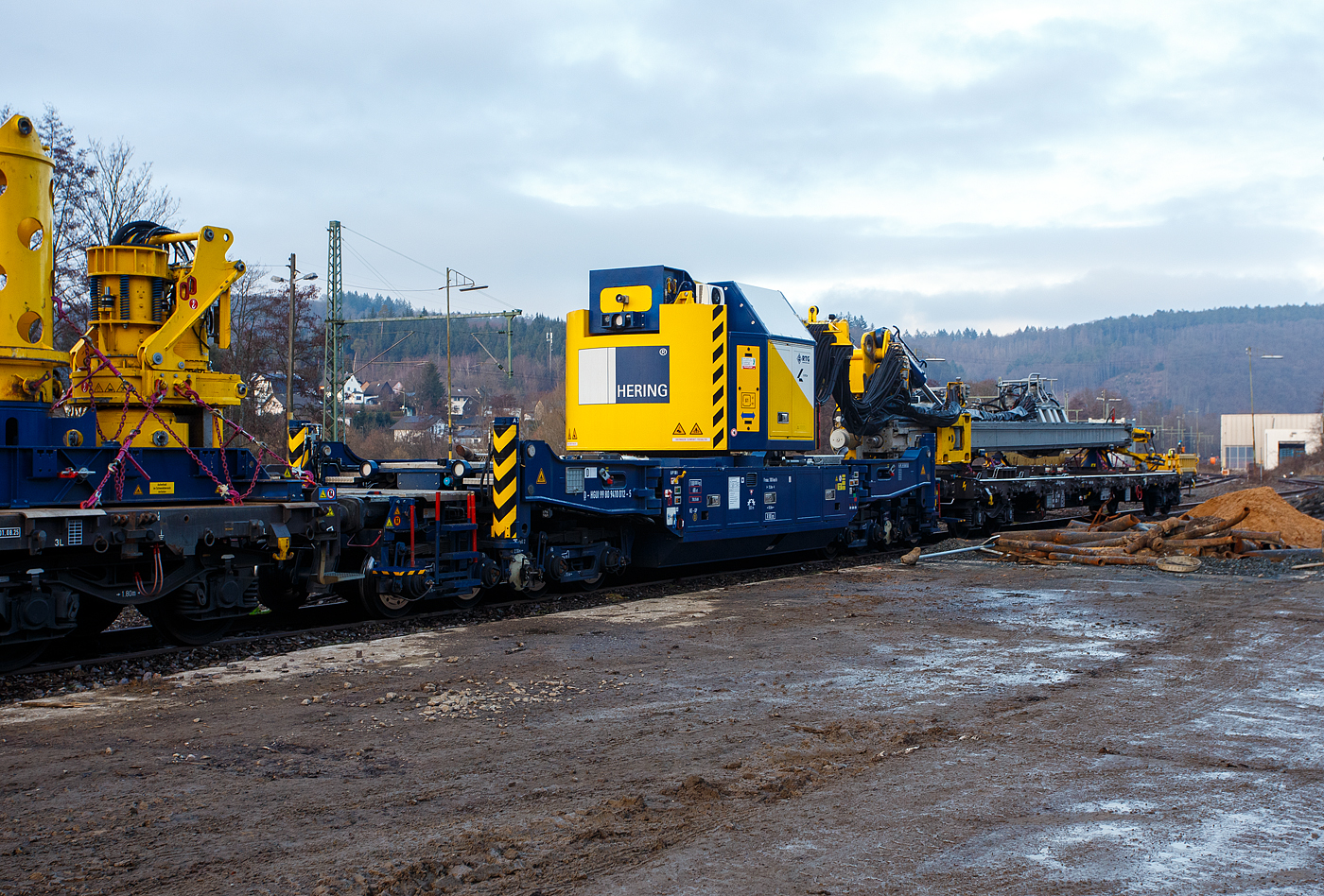 Der Gleisgründungszug der HERING Bahnbau GmbH (Burbach-Holzhausen) ist am 05 Februar 2026 auf den WEBA-Gleisen in Scheuerfeld/Sieg abgestellt. Hier das 8-achsigen gleisgebundenen Trägergerät (Baujahr 2023 durch TECHNE KIROW GmbH in Leipzig unter Fabriknummer MT 2020 171031), D-HGUI 99 80 9410 012-5, Gewicht 108.000 kg, LüP 15.000 mm. Davor der Flachwagen zur Ablage des Mäklers (der Führungseinrichtung), 37 80 3981 003-1 D-HGUI, der Gattung Rnps (ex Rens 192B), LüP 19.900 mm

Die Höchstgeschwindigkeit beträgt 100 km/h geschleppt, bei Eigenfahrt 5 km/h. 