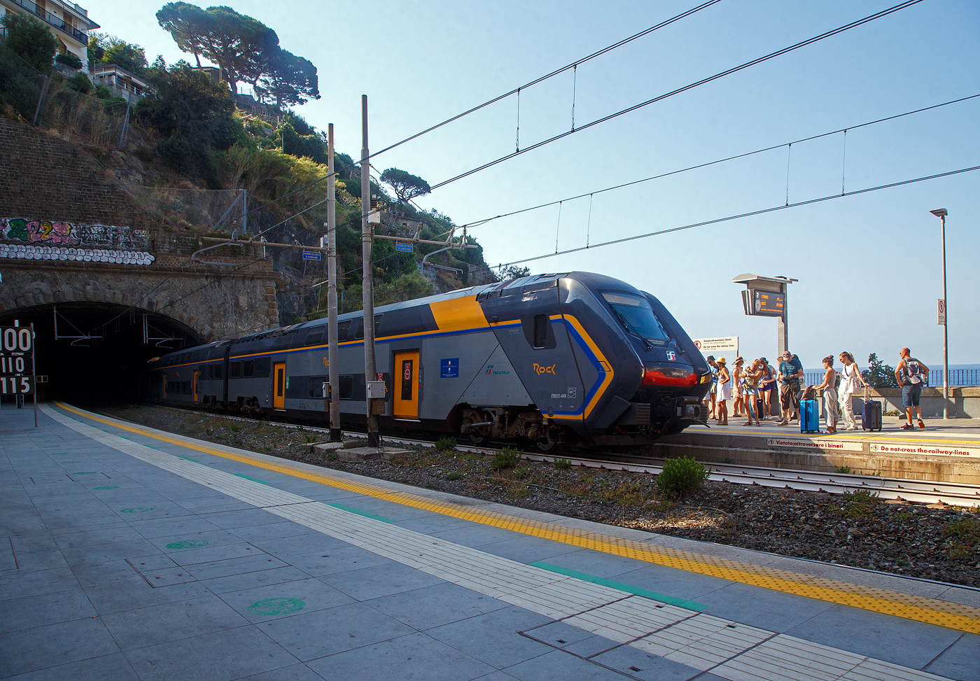 Der Trenitalia “Rock” ETR 521-048, ein fünfteiliger Elektrotriebzug vom Typ Hitachi Caravaggio, erreicht am 22.07.2022 den Bahnhof Riomaggiore (Cinque Terre). Er fährt als Cinque Terre Express (Regionale) von La Spezia Levanto, via Riomaggiore, Manarola, Corniglia, Vernazza, Monterosso, nach Levanto.

Die Züge des Cinque Terre Express, obwohl sie alle ¼ Stunde fahren, sind immer sehr gut gefüllt. Nicht immer findet man einen Sitzplatz. Für die Fahrt mit den Cinque Terre Express muss man ein spezieles Ticket lösen, z.B. Trenitalia nationale Tageskarten gelten hier nicht. 

Wer wie wir die Cinque Terre Card Treno (Zugkarte) besitzt, kann dann auch mit den Minibusen des Cinque Terre Parks (im Preis der Cinque Terre Treno Card eingeschlossen) in den fünf Dörfern kostenlos fahren. Zudem hat man mit dieser Karte auch Zutritt zu den beiden gebührenpflichtigen Wanderwegen des Cinque Terre Parks.