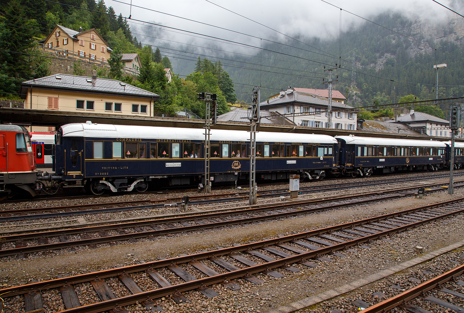 Der VSOE Schlafwagen Nr. 3553 – VSOE Voiture-Lits / Carrozza-Letti N° 3553 (F- VSOE 61 87 06-70 553-9 [P]) im Zugverbund vom Venice Simplon-Orient-Express am 02 August 2019 beim Halt im Bahnhof Göschenen (CH), leider bei Regen.

Der Schlafwagen, wurde 1929 von EIC - Entreprises industrielles des Charentes (EIC, heute zu Alstom gehörend) in Aytré (F), als CIWL Typ Lx 18 (Schlafwagen mit Schlafwagenschaffnerabteil), gebaut und als Schlafwagen Nr. 3553 an die CIWL - Compagnie Internationale des Wagons-Lits geliefert. 1943 wurde er zum in den Typ LX 20 (zehn Zweibettabteile) umgebaut. Im Jahr 1980 wurde er an die VSOE (Venice Simplon-Orient-Express Ltd.) verkauft. Hier wurde der Wagen überholt und technisch modernisiert, unter anderem mit Klimaanlagen. Bei den VSOE-Wagen wurde ein Schlafwagenabteil zum Abteil für den Schlafwagenschaffner hergerichtet, die Wagen werden seitdem (wieder) als Typ Lx 18 bezeichnet. 

Zwischen 2003 und 2006 wurde die Wagen der VSOE wieder modernisiert und erhielten unter anderem moderne Drehgestelle von Bombardier sowie neue Klimaanlagen. Durch die neuen Drehgestelle sind die Wagen seitdem für 160 km/h zugelassen. 

TECHNIK
Mit der Einführung von Ganzstahlwagen ging die CIWL dazu über, von Ausnahmen abgesehen alle Fahrzeuge auf einem einheitlichen Rahmen mit 23.452 mm Länge über Puffer und einem Drehzapfenabstand von 16.000 mm aufzubauen. Die Fahrzeugbreite beträgt 2.850 mm, die Höhe über Schienenoberkante 4.000 mm. Auf dieser Basis entstanden neben dem Typ Lx auch die Schlafwagen der Typen S, Y und Z. Die gleichen Rahmen wurden auch für Speisewagen und Pullmanwagen verwendet, sie bestehen aus drei Längsträgern mit Querverbindungen und zwei Gussstahlblöcken an den Enden zur Aufnahme der Zug- und Stoßvorrichtungen. Auf dem Rahmen sind die Seitenwände und Fußböden sowie die beiden Zustiegsplattformen aufgebaut. Das Gewicht des Typs Lx beläuft sich auf 53 Tonnen (heute 57 t). Als Drehgestelle erhielten die Wagen ursprünglich Schwanenhals-Drehgestelle mit Rollenlagern, auch als Pennsylvania-Drehgestelle bezeichnet. Im Laufe der Jahre wurden diese teilweise durch neuere Drehgestelle oder andere Bauarten ersetzt. Ursprünglich waren die Wagen lediglich für 130 km/h zugelassen, nach dem Krieg wurde die Geschwindigkeit auf 140 km/h angehoben. Die mit neuen Drehgestellen modernisierten Wagen des VSOE sind für 160 km/h zugelassen.

Die CIWL rüstete alle Wagen neben einer über die Heizdampfleitung des Zuges versorgten Dampfheizung mit einer unabhängig zu betreibenden Kohleheizung aus, die durch den Schlafwagenschaffner bedient wurde und bei längerem Stillstand eines Zuges zum Einsatz kam. In den Nachkriegsjahren erhielten viele Fahrzeuge außerdem elektrische Heizleitungen. In jedem Abteil befand sich zur Belüftung ein Ventilator, die Wagen der VSOE wurden mit Klimaanlagen ausgerüstet.

Es gab kein gesondertes Abteil für den Schlafwagenschaffner, dieser nächtigte auf einer an einem Ende des Wagens aufgeklappten Liege im Gang. Vorräte für die Versorgung der Fahrgäste befanden sich in Schränken an den Wagenenden. An einem Ende war ein WC untergebracht. Jeweils zwei der Abteile (mit Ausnahme der beiden äußersten Abteile) ließen sich mittels einer verschließbaren Tür zu einer größeren Suite verbinden. Die in den historischen Luxuszügen eingesetzten, noch erhaltenen Wagen des Typs sind teils umfassend modernisiert und umgebaut worden. Bei den im VSOE eingesetzten Wagen wird eines der Abteile für den Schaffner genutzt. Die Wagen besitzen zudem moderne Klimaanlagen.

TECHNISCE DATEN:
Spurweite: 1.435 mm (Normalspur)
Anzahl der Achsen: 4 in zwei Drehgestellen
Länge über Puffer: 23.452 mm
Drehzapfenabstand: 16.000 mm
Achsabstand im Drehgestell: 2.500 mm
Eigengewicht: 57 t
Höchstgeschwindigkeit: 160 km/h (ursprünglich 140 km/h)
Betten- und Sitzplätze: 18 (in 9 Zweibettabteilen) plus Schaffnerabteil 

DER HEUTIGE WAGEN 3553 - L'Observatoire
Im Jahr 2023 entwarf französische Künstler JR das Innere des neuen Privatwagens 3553 - L'Observatoire (Privatwagen) des Venedig Simplon-Orient-Express, der so 2023/24 umgebaut wurde und nun die UIC-Nummer F- VSOE 61 87 76-70 000-6 [P] trägt. Jetzt ist es ein Privatwagen mit einem Schlafzimmer für zwei Personen, einem Wohnzimmer, einer Bibliothek, einer Teekammer und einem Badezimmer mit freistehender Badewanne. Das Fahrzeug wurde im April 2024 auf der Biennale in Venedig ausgestellt, um erste Eindrücke zu liefern, und es läuft seit 2025 im Zug des Venice Simplon-Orient-Express. Ich würde ich gerne mal selbst von innen sehen. 

L’Observatoire, das sich über einen ganzen Wagen an Bord des Venedig Simplon-Orient-Expresss entfaltet, ist ein einzigartiger Raum, um Neugier, Abenteuer und Kreativität zu genießen. Inspiriert von astronomischen Observatorien hat der Künstler JR eine wagengroße Suite entworfen, er soll ermutigen, zu blicken, hinaus und darüber hinaus - und zwar mit Handwerkskunst sowohl von alten Meistern als auch von aufstrebenden Wegbereitern harmonieren. Wenn man das nötige Kleingeld hat😉.

In einem 23 Meter langen Raum entfalten sich die Innenräume des Wagens in mehreren Umgebungen, von einem Schlafzimmer mit einer freistehenden Badewanne bis zu einer Bibliothek voller Gallimard-Bücher. Wenn man den Korridor entlang schlendert, kann man die ausgestellte JR-Fotografie bewundern. Ein Plattenspieler mit einer kuratierten Vinyl-Sammlung ist als Soundtrack zum außergewöhnlichen Abenteuer auch dabei.

Zudem heißt es: Enthüllen Sie handgefertigte Intarsien, Glasmalereien und sogar einen Miniatur-Zugwagen, der von einem Modellbaumeister aus der Schweiz geschaffen wurde. Schauen Sie näher, um eine Welt von Feiernden zu entdecken, die auf winzigen Bildschirmen im Inneren des Modells laufen. Entdecken Sie die versteckte Teestube, ein kreisförmiges Refugium, in dem Sie Momente stiller Kontemplation genießen können. Dieser exklusive Raum ist nur für Ihre Augen reserviert. Schließlich schauen Sie auf, um einen Oculus zu enthüllen und den Himmel zu bestaunen.
