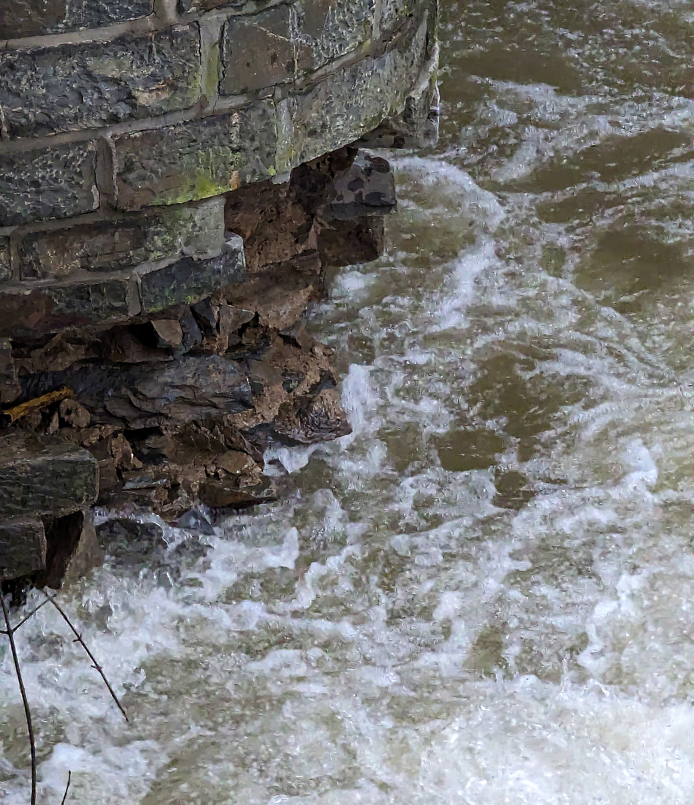 Detailbild (mit Smartphone) von dem betroffenen Fundament des Brückenpfeilers der Eisenbahn-Siegbrücke mit Fußgängersteg in Kirchen (Sieg), der KBS 460 Siegstrecke. Wie weit der Schaden im/unter Wasser ist kann man nicht erkennen, aber ich würde es auch nicht verantworten wollen. Hier am 03.01.2024.