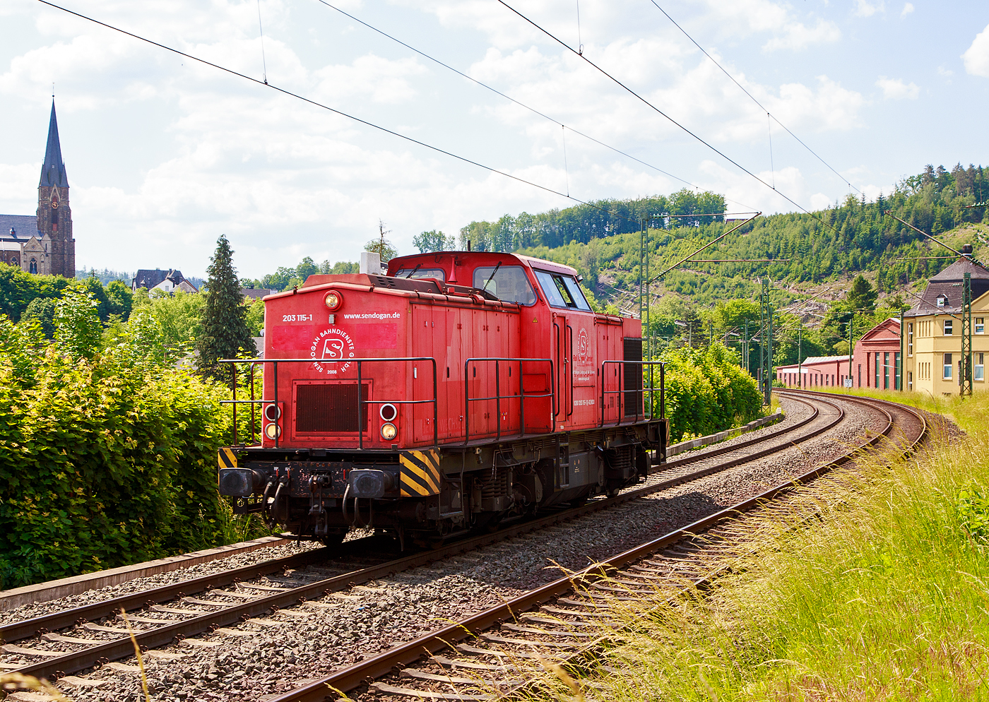 Die 203 115-1 (92 80 1203 115-1 D-SENDO) der Sendogan Bahndienste GmbH (Recklinghausen), ex DB 202 450-3, fährt am 06.06.2023 als Lz (Lokzug) bzw. auf Tfzf (Triebfahrzeugfahrt) Kirchen an der Sieg in Richtung Siegen. Übrigens recht in den Fabrikhallen wurde früher auch Loks gebaut, es ist die Lokfabrik Arnold Jung in Jungenthal bei Kirchen an der Sieg.

Die V 100.1 wurde 1972 bei LEW (VEB Lokomotivbau Elektrotechnische Werke „Hans Beimler“, Hennigsdorf) unter der Fabriknummer 13489 gebaut und als DR 110 450-4 an die DR ausgeliefert. 1984 erfolgte der Umbau in DR 112 450-2, die Umzeichnung in DR 202 450-3 erfolgte 1992, die Ausmusterung bei der DB erfolgte 1998. Im Jahre 2002 erfolgte durch ALSTOM Lokomotiven Service GmbH, Stendal der Umbau gemäß Umbaukonzept  BR 203.1  in die heutige 203 115-1, die Inbetriebnahme war im Jahr 2005. Von 2005 bis Dezember 2010 war die Lok von ALSTOM Lokomotiven Service GmbH wieder an die DB (DB Regio bzw. DB Schenker) vermietet, bis sie Anfang 2011 an die EBM verkauft wurde. 2015 wurde die EBM Cargo GmbH von der Rail Cargo Carrier - Germany GmbH (zur ÖBB) übernommen, somit wurde die Lok zur 92 80 1203 115-1 D-RCCDE. Im Mai 2021 ging sie an die Sendogan Bahndienste GmbH in Recklinghausen.

TECHNISCHE DATEN:
Spurweite: 1.435 mm (Normalspur)
Achsanordnung: B'B'
Länge über Puffer: 14.240mm
Radsatzabstand im Drehgestell: 2.300mm
Drehzapfenabstand: 7.000mm
Höhe über SO: 4.255mm
Dienstgewicht: 69 t

Motor: 12-Zylinder CATERPILLAR-Dieselmotor mit Direkteinspritzung, Abgasturbolader und Ladeluftkühlung, vom Typ CAT 3512 DI-TA
Motorleistung: 1.305 kW (1.774 PS)
Nenndrehzahl: 1.800 U/min
Hubraum: 51,8 Liter (Bohrung-Ø 170 x Hub 190 mm)
Motorgewicht: 6.537 kg

Getriebe: Voith Strömungsgetriebe GSR 30/5,7
Leistungsübertragung: dieselhydraulisch
Anfahrzugkraft: 207 kN
Höchstgeschwindigkeit: 100 km/h
Kleinste Dauerfahrgeschwindigkeit: 11,1 km/h
Kleinster befahrbarer Gleisbogenradius: 80m
