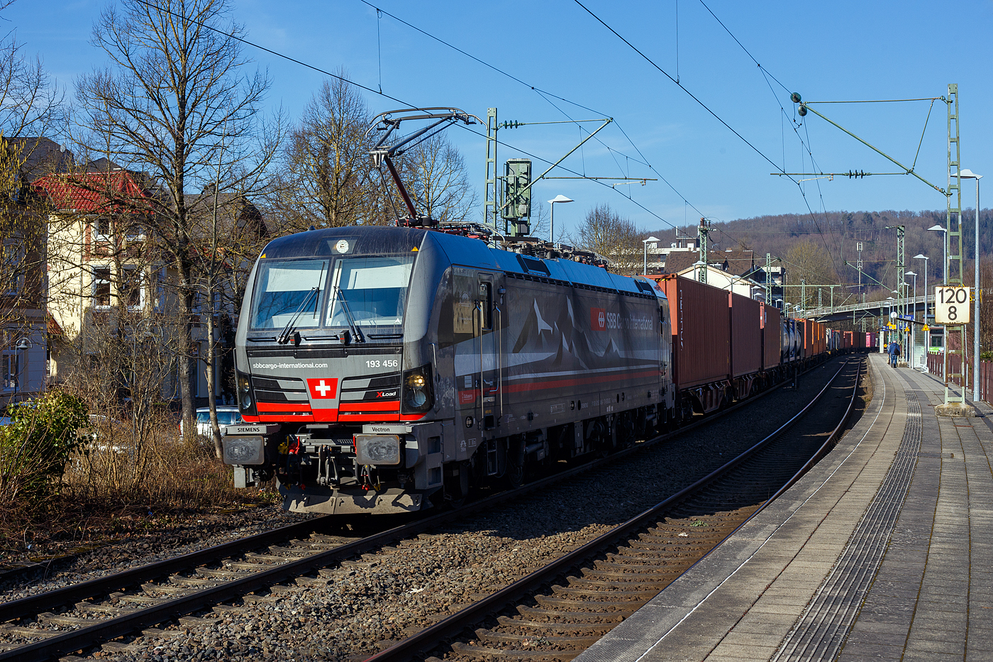 Die an die SBB Cargo International AG vermietete mit „XLoad“ ausgestattete 193 456  Schweizer Bahnhof Basel  (91 80 6193 456-1 D-SIEAG) der SüdLeasing GmbH, Stuttgart (eingestellt in Deutschland durch Siemens) fährt am 18 Februar 2025 mit einem KLV-Zug, durch Kirchen (Sieg) in Richtung Köln.

Die Multisystemlokomotive Siemens Vectron MS wurde 2024 von Siemens Mobilitiy in München-Allach unter der Fabriknummer 23784 gebaut und am 12.09.2024 ausgeliefert. Sie wurde in der Variante A40-1a ausgeführt und hat so die Zulassung für Deutschland, Österreich, die Schweiz, Italien, die Niederlande und Belgien (D / A / CH / I / NL / B). Sie verfügt über eine Leistung von 6,4 MW (160 km/h) und ist neben den nationalen Zugsicherungssystemen mit dem Europäischen Zugsicherungssystem (ETCS BL3) ausgestattet. Zudem ist sie mit der neuen Ausrüstungspaket XLoad ausgestattet. 

Das neue XLoad Ausrüstungspaket für Vectron:
XLoad ist ein Ausrüstungspaket für Vectron, welches künftig mitbestellt, aber auch bei bereits ausgelieferten Vectron Loks nachgerüstet werden kann. Das Feature verbessert die Reibwertausnutzung und ermöglicht dadurch höhere Anhängelasten. Zudem reduzieren die Fahreigenschaften, die das Feature bewirken, den Verschleiß von Rad und Schiene.

Aktuell sind die Schweizer Vectron-Lokomotiven (SBB Cargo und BLS Cargo) in der Regel in Doppeltraktion unterwegs. Die Steigungen und Rampen der Schweizer Berge sind vor allem bei schlechten Witterungsbedingungen nicht ohne. Eine Lokomotive muss auch bei geringerem Schlupf genügend Traktion auf die Schienen bringen, um alle Güter sicher und zuverlässig ans Ziel zu bringen. Ein effizienter Weg aus dieser «Misere» ist die für Vectron entwickelte Zusatz-Funktion «XLoad». Den erfolgreichen Beweis trat eine SIEMENS Testlokomotive im Frühjahr 2022 bei der SBB Cargo International und bei der BLS Cargo eindrücklich an. 

Für SBB Cargo International bewies die Test-Lokomotive am Bözberg und für BLS Cargo an der Nordrampe des Lötschbergs ihre enorme Zugkraft. 
Vectron meisterte im Frühjahr 2022 die lange 12‰-Steigung des Bözbergs mit einer Anhängerlast von 2.000 Tonnen bravourös. Bei den nächtlichen Testfahrten zeigte sich eindrücklich die enorme Zugkraft der Lokomotive. 

Am Lötschberg wurden bei der BLS Cargo steigungsmäßig noch ein paar Promille draufgepackt. Mit 1.020 Tonnen im Gepäck bewältigte die Vectron-Lokomotive mit XLoad-Feature die 27‰-Steigung der Nordrampe ebenfalls meisterlich. Und auch diverse Anfahrtsversuche absolvierte der mit dem XLoad-Feature aufgerüstete Vectron problemlos. 

So bestellte die SüdLeasing GmbH (Stuttgart) im Auftrag der SBB Cargo International jüngst 20 Vectron Lokomotiven mit XLoad bei SIEMENS.