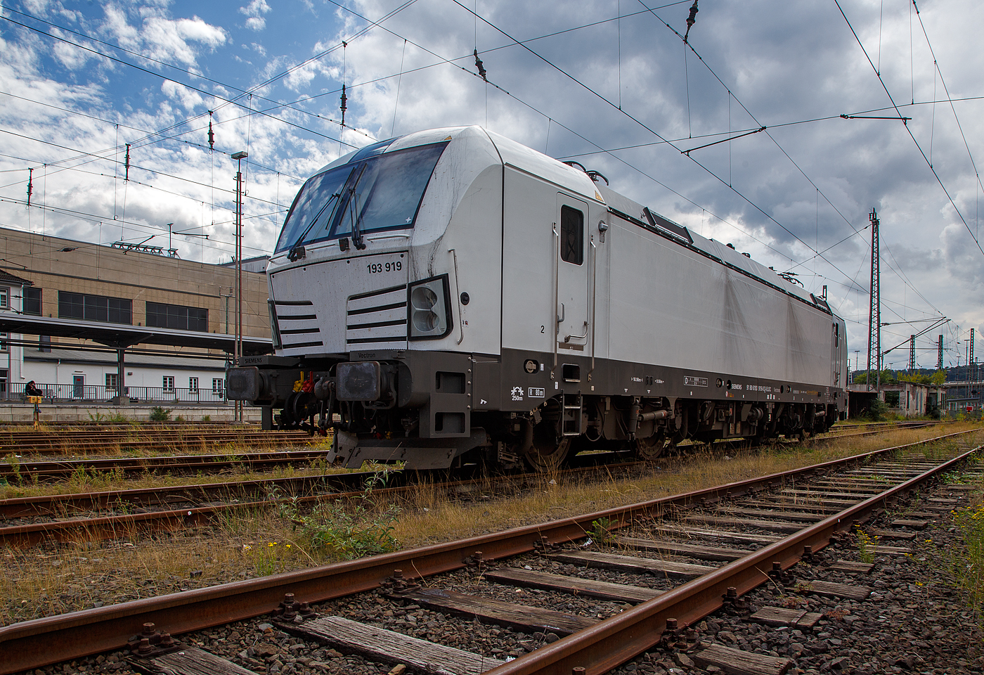 Die an die SETG - Salzburger Eisenbahn TransportLogistik GmbH vermietete weiße SIEMENS Vectron AC DPM 193 919 (91 80 6193 919-8 D-ELOC) der ELL - European Locomotive Leasing ist am 28.08.2023 beim Hbf Siegen abgestellt.

Die SIEMENS Vectron AC DPM mit Diesel Power Modul  bzw. mit LM (Last Mile Diesel) wurde 2022 von Siemens Mobilitiy in München-Allach unter der Fabriknummer 22968 gebaut. Diese Vectron Lokomotive ist als AC DPM – Lokomotive (Wechselstrom-Variante mit Dieselmodul für Rangieren ohne Fahrdraht) mit 6.400 kW konzipiert und zugelassen für Deutschland, Österreich, Bulgarien, Slowakei, Rumänien, Tschechien und Ungarn (D/A/BG/SK/RO/CZ/H), im Dieselbetrieb beträgt die Leistung lediglich 180 kW (160 kW am Rad). 

Diese topmodernen Lokomotiven weisen eine Leistung von 6.400 kW (8.700 PS) auf. Das eingebaute Diesel-Power-Modul ermöglicht das Rangieren ohne Fahrdraht. Zusätzlich sind die Vectron-Lokomotiven von Siemens mit einer Funkfernsteuerung und einer halbautomatischen Bremsprobe ausgerüstet. 

Die Entwicklung der Siemens Lokomotive Vectron basiert auf den Erfahrungen der erfolgreichen EuroSprinter beziehungsweise deren Weiterentwicklung Siemens ES 2007 (NMBS/SNCB-Reihe 18/19) ersetzt. Ausgereifte und bewährte Technik ist mit Flexibilität und Modularität kombiniert. Die Vectron Lokomotive ist für die vielfältigsten Verkehrsaufgaben konzipiert. Ob im nationalen oder grenzüberschreitenden Verkehr, ob im Personen- oder Güterverkehr. Es werden vier elektrische Versionen und eine dieselelektrische Version der Lokomotivplattform angeboten. Die hier gezeigten Vectron Lokomotiven sind als AC – Lokomotiven (Wechselstromlok) mit 6.400 kW Leistung) konzipiert und haben ein Diesel Power Modules (DPM) / Rangiermodul bzw. Last Mile (LM).

Die äußere Gestaltung der Vectron-Lokomotiven unterscheidet sich nur wenig von der der Siemens ES 2007; insbesondere wird das der Crashnorm entsprechende Kopfmodul bis auf einige Detailänderungen, etwa Rückblickkamera statt Seitenfenster, übernommen. Innen ist der neue Typ hingegen komplett anders aufgebaut. Der Maschinenraum besitzt im Gegensatz zur Bombardier TRAXX einen geraden Mittelgang, an dessen Seiten alle Komponenten einen festen Platz haben. In einem unter dem Boden verlaufenden Kanal verlaufen die Steuerleitungen und Druckluftrohre. Die Radsätze werden über gefederte Ritzel-Hohlwellen angetrieben.

Der Vectron unterstützt mit einer optimierten Systemauslegung und vielfältigen Funktionen für energieoptimales Abstellen. Der elektrische Vectron ermöglicht eine erhöhte elektrische Bremskraft von 240 kN. Die rückgewonnene Energie wird hocheffizient für die Versorgung von Hilfsbetrieben genutzt bzw. und wo möglich ins Netz zurückgespeist.

TECHNISCHE DATEN der Vectron AC DPM:
Spurweite: 1.435 mm
Achsformel: Bo'Bo'
Länge über Puffer: 18.980 mm
Drehzapfenabstand: 9.500 mm
Achsabstand im Drehgestell: 3.000 mm
Breite: 3.012 mm
Höhe: 4.248 mm
Raddurchmesser : 1.250 mm (neu) / 1.160 mm (abgenutzt)
Gewicht: 90 t
Spannungssysteme: 15 kV, 16,7 Hz AC (Wechselstrom)
Max. Leistung am Rad: 6.400 kW
Leistungsfaktor: nahe 1
Höchstgeschwindigkeit: 160 km/h
Anfahrzugskraft: 300 kN
Dauerzugkraft: 250 kN
Elektrische Bremskraft: 240 kN
Kraftübertragung: Ritzelhohlwellenantrieb
Lichtraumprofil: UIC 505-1

Leistungsdaten DPM (Diesel Power Modul):
Max. Geschwindigkeit : 40 km/h
Leistung: 180 kW (160 kW am Rad)
Tankvolumen der DPM:  350 l (Diesel)
