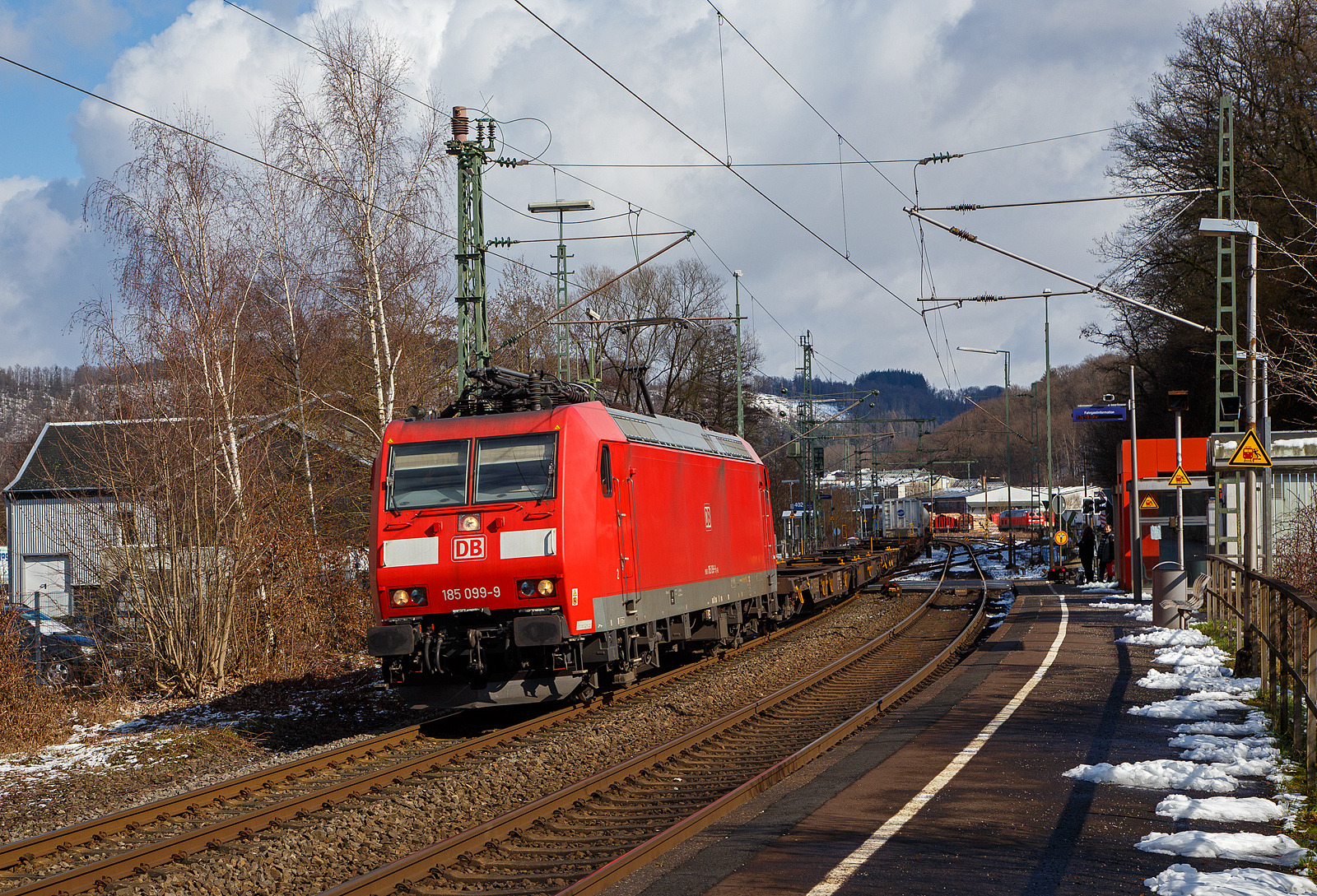 Die auch für die Schweiz zugelassene 185 099-9 (91 80 6185 099-9 D-DB) der DB Cargo AG fährt am 15.03.2023, mit einem KLV-Zug auf der Siegstrecke (KBS 460) durch Scheuerfeld (Sieg) in Richtung Köln.

Die TRAXX F140 AC1 wurde 2002 von der Bombardier in Kassel unter der Fabriknummer 33521 gebaut. Sie hat die Zulassung für Deutschland und die Schweiz, man kann es auch an den vier DSA-200 Einholm-Stromabnehmer erkennen. Außen sind jeweils die für das Schweizernetz bestimmten Stromabnehmer mit einer 500 mm schmaleren Wippenbreite von 1.450 mm und innen die DB-Netz bestimmten mit einer Wippenbreite von 1.950 mm.