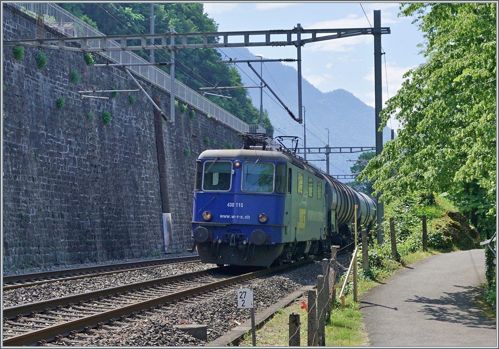 Die ehemalige SMB Re 4/4 181 ist heute als WRD Re 430 115 unterwegs; beim Château de Chillon im ungünstigen Gegenlicht auf der Fahrt in Richtung Lausanne. 

31. Mai 2023