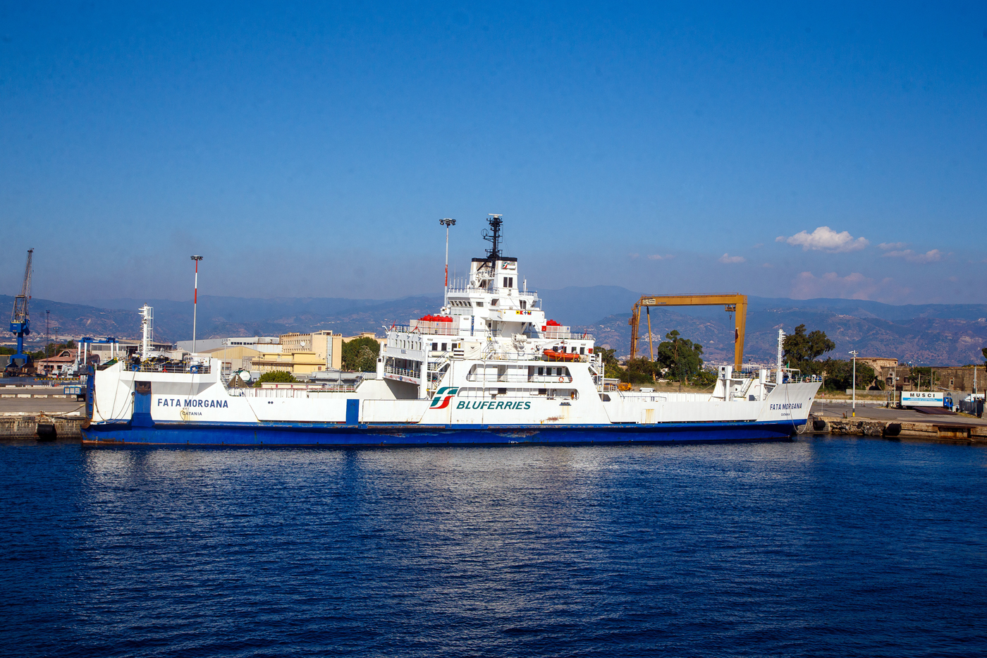 Die FATA MORGANA (IMO 8506543) ein Ro-Ro Fährschiff der Bluferries (ein Unternehmen der Gruppe FS - Ferrovie dello Stato Italiane), liegt am 20.07.2022 beim Fährterminal von Messina. Diese Fähre ist für die Beförderung von Passagieren und Radfahrzeugen in der Straße von Messina. Sie kann aber auch Eisenbahnwaggons transportieren (Trajekt). 

TECHNISCHE DATEN:
Bauwerft: Fincantieri – Cantieri Navali Italiani S.p.A. in Livorno, Italien
Kiellegung/Stapellauf: 1887 / 1988
Inbetriebnahme: 1989
Vermessung (Bruttoraumzahl): 2.377 BRT
Länge: 102 m
Breite: 18,82 m
Tiefgang: 4,5m
Antrieb: 2 GMT(Grandi Motori Trieste) 4-Zylinder-Dieselmotoren mit einer Leistung von 10.357 kW
Geschwindigkeit: 15,2 Knoten (28,15 km/h)
Ladekapazität: 79 Autos oder 24 LKW oder 12 Eisenbahnwaggons
Besatzung: 10
Zugelassene Passagierzahl: 500 
