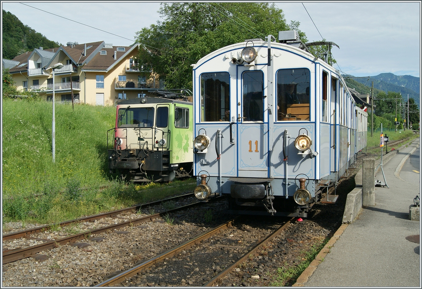 Die Front der in Blonay abgestellte MOB GDe 4/4 6006 bietet einen schönen Hintergrund zum einfahrenden MOB BCFe 4/4 N° 11 der Blonay Chamby Bahn, der mit dem letzten Zug des Tages in den Bahnhof einfährt. 

13. Juli 2024 