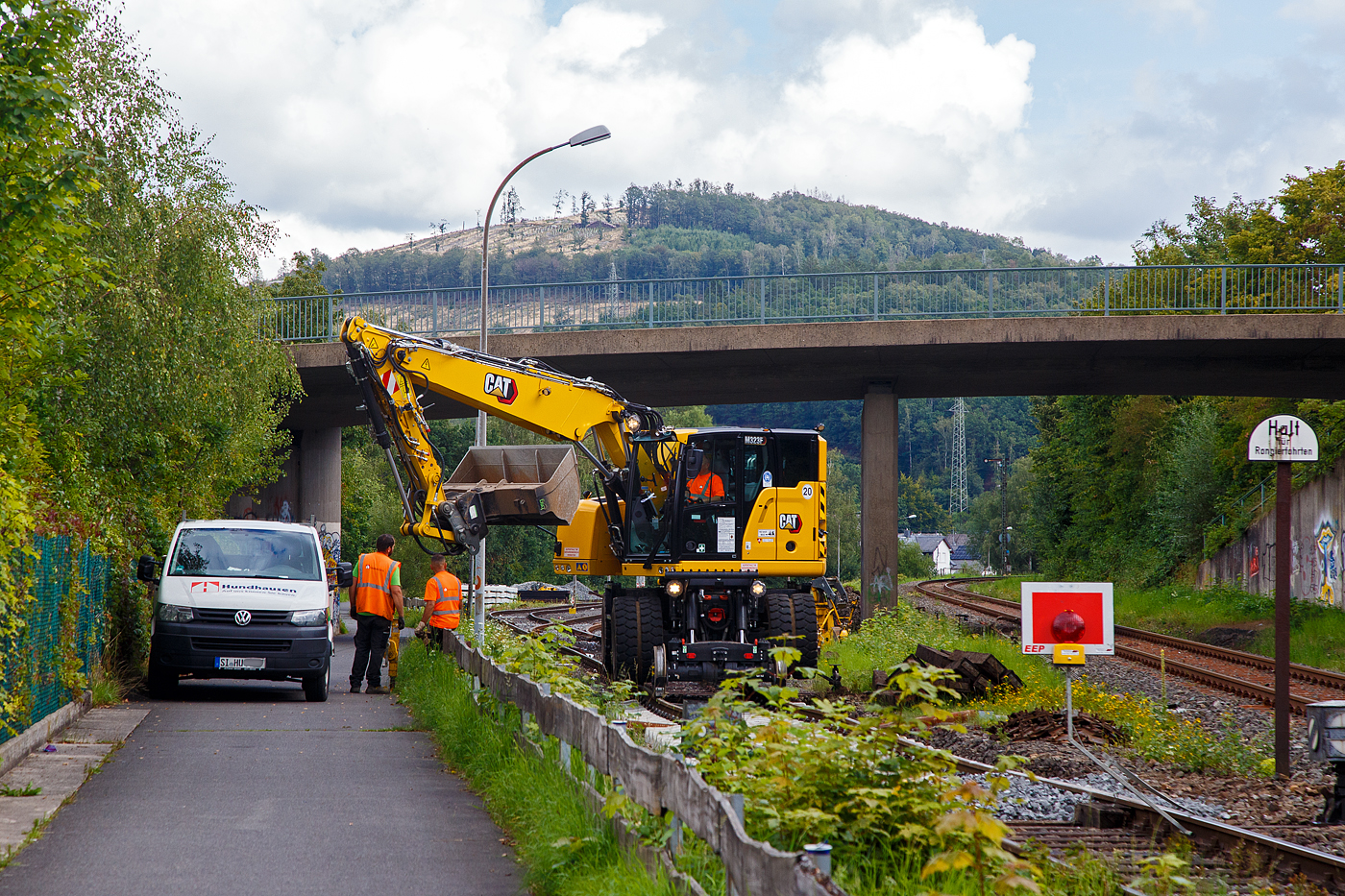 Die KSW (Kreisbahn Siegen-Wittgenstein) erneuert die ersten Gleismeter vom Anschlussgleis, zum Rangierbahnhof in Herdorf der Betriebsstätte FGE -Freien Grunder Eisenbahn (KSW NE447 / DB-Nr. 9275).

Hier am 16.08.2023 im Einsatz der Caterpillar CAT M323F Zweiwegebagger mit hydrostatischem Schienenradantrieb (Serien-Nr. RH600 189), Kleinwagen Nr. D-ZBM 99 80 9902 521-0 der ZEPPELIN Baumaschinen GmbH (Garching), ein Mietbagger vermietet an die Firma  W. Hundhausen Bauunternehmung GmbH (Siegen). Es werden die ersten Gleismeter vom Anschlussgleis erneuert, der Bagger ist bei der Einschotterung.
