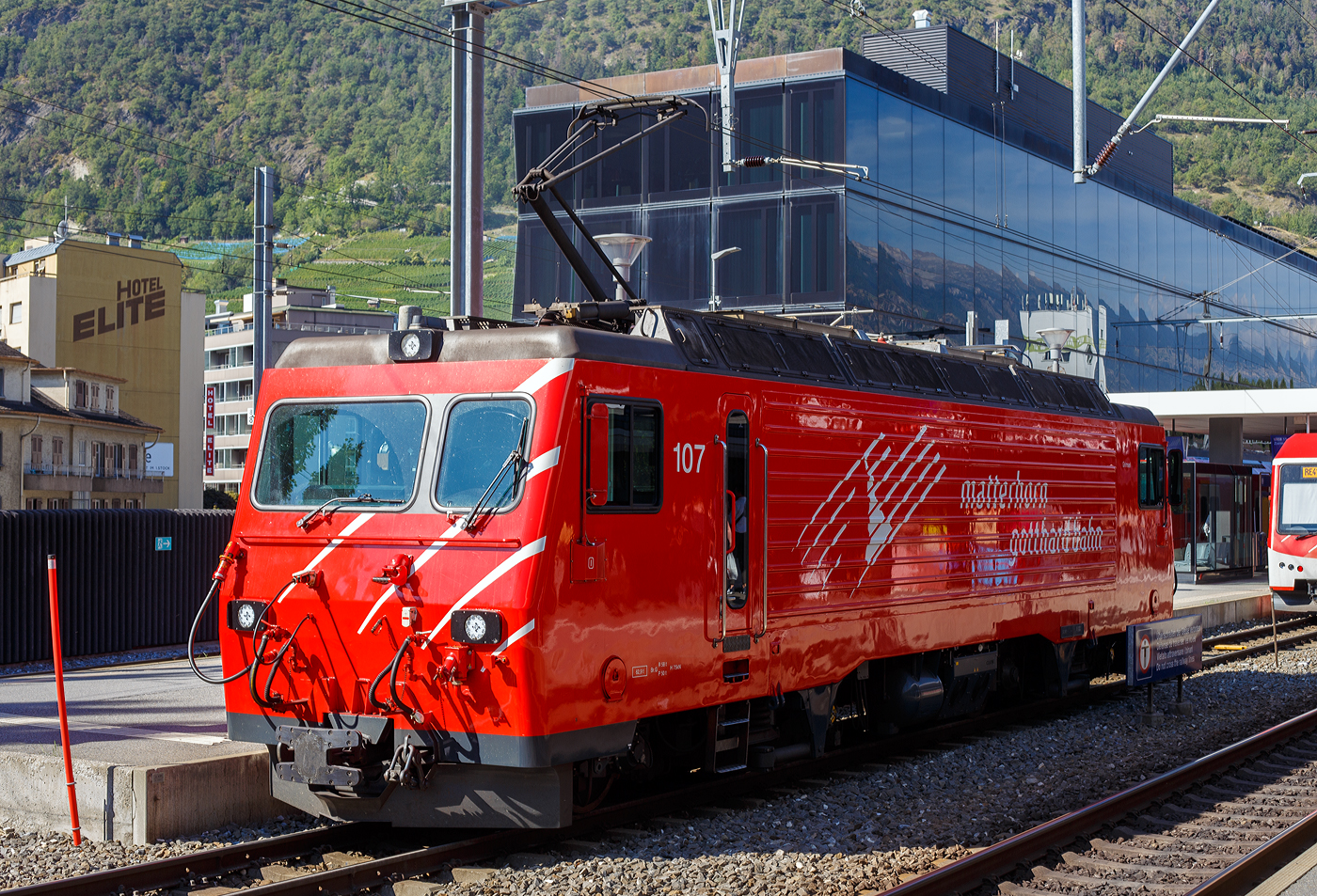 Die MGB HGe 4/4 II 107 „Grimsel“ erreicht am 11 September 2022 als Lz (solo) den Bahnhof Visp.

Die HGe 4/4 II 103 „Grimsel“ wurde 1990von der SLM (Schweizerische Lokomotiv- und Maschinenfabrik) in Winterthur unter der Fabriknummer 5393 gebaut und an die FO (Furka-Oberalp-Bahn) geliefert. Der elektrische Teil ist von BBC. 

Die HGe 4/4 II ist eine schmalspurige (1.000 mm) gemischte Zahnrad- und Adhäsions-Lokomotive. Eine erste Serie von fünf Lokomotiven wurde gemeinsam von der Furka-Oberalp-Bahn (FO) sowie von der SBB für die Brünigbahn, die heute zur Zentralbahn (zb) gehört, beschafft. Da sich dieser Lokomotivtyp bewährte, wurden weitere elf Lokomotiven bestellt, und schließlich gab auch noch die Brig-Visp-Zermatt-Bahn (BVZ) fünf Loks in Auftrag.

Die HGe 4/4 II bespannt vor allem schwere Personenzüge, zum Teil im Pendelzugbetrieb. Bei der Zentralbahn bespannte sie bis 2012 alle Schnellzüge von Meiringen nach Luzern, bei der Matterhorn Gotthard Bahn die Züge des Glacier-Express. Weiter führen die Loks Pendelzüge Brig–Visp–Zermatt und seit der Eröffnung des Tunnels nach Engelberg Pendelzüge Luzern–Engelberg. Außerdem werden aushilfsweise Autopendelzüge durch den Furkatunnel geführt. Schließlich gehören neben weiteren Personenzügen auch diverse Güterzüge Visp–Zermatt sowie bis 2013 Disentis–Sedrun (NEAT-Baustelle) zum Aufgabengebiet.

Konstruktion:
Der Lokomotivkasten ist ein Stahlblechkasten mit gesickten Seitenwänden. Die asymmetrische Frontscheibe aus beheizbarem Verbundglas verbessert die Sicht für den Lokomotivführer. Die drei Dachelemente sind aus Aluminium. Die Pufferkräfte werden über Verstrebungen auf den ganzen Kasten übertragen, weshalb auf seitliche Maschinenraumöffnungen verzichtet werden musste. Der gesamte Kasten hat ein Gesamtgewicht von nur 5,9 Tonnen. Er kann ohne bleibende Deformation eine zentrale Druckkraft von 1000 kN aufnehmen.

Die Drehgestelle sind als geschweißte Hohlträgerkonstruktion mit zwei Längsträgern und einem kräftigen mittleren Querträger sowie zwei Kopftraversen ausgeführt. Sie haben einen Achsstand von 2980 mm, und die Flexicoil-Federn stützen den Kasten auf die seitlich an die Längsträger angeschweißten Federwannen. Die Zug- und Druckkräfte werden durch seitlich angeordnete Stangen mit Sphärolastiklagern übertragen. Wegen des kurzen Achsstands sind die Fahrmotoren oberhalb des Drehgestellrahmens angebracht.
Für den Antrieb wurde erstmals der Differentialantrieb eingebaut, der es ermöglicht, im Zahnstangenbetrieb auch einen Anteil der Zugkraft über den Adhäsionsantrieb aufzubringen. Dies setzt wiederum eine Schlupfbegrenzung im Differentialgetriebe voraus, um ein Schleudern oder Gleiten der Räder zu verhindern. Da die zweilamellige Abtzahnstange (System Abt) der FO nicht die gesamte Zugkraft aufnehmen kann, ist die Mithilfe des Adhäsionsantriebs notwendig; dieser übernimmt einen Drittel der Zugkraft. Hätte sich der Antrieb nicht bewährt, wäre es zumindest am Brünig mit der Riggenbachzahnstange möglich gewesen, auf einen abkuppelbaren Adhäsionsantrieb zu wechseln. Dies war aber nicht notwendig, da das Differentialgetriebe zur vollen Zufriedenheit funktionierte.

Bremssysteme:
Dank der elektrischen Rekuperationsbremse ist eine gleichmäßige Beharrungsbremse bei der Talfahrt möglich.
Daneben ist eine normale automatische Druckluftbremse eingebaut, welche auch als Bremssystem I bezeichnet und im Regelbetrieb zum Halten des Zuges verwendet wird. Sie ist als Klotzbremse ausgeführt.
Weiterhin ist noch das Bremssystem II installiert, welches für Zahnradbahnen vorgeschrieben ist und es ermöglichen soll, den Zug nur mit Hilfe der Lokomotive im Zahnstangenabschnitt zum Halten zu bringen, wenn das erste Bremssystem ausfallen sollte. Dieses ist als federspeichergestütztes Bandbremssystem ausgelegt, welches direkt auf das Zahnrad wirkt. Bei Einsatz dieser Bremse treten enorme Kräfte auf, welche nur unter Kontrolle sind, wenn die Anhängelast bei der Talfahrt nicht zu groß ist.
Schließlich ist eine direkt wirkende Rangierbremse vorhanden, die sich der Bremsklötze des Bremssystems I bedient.
Die Lokomotive hat keine Handbremse, sondern wird mit Federspeicherbremsen gesichert.

TECHNISCHE DATEN der HGe 4/4 II der FO und BVZ (heute MGB), 
die Daten der  zb (Zentralbahn), ex SBB Brünigbahn weichen ab:
Spurweite: 1.000 mm
Achsformel: Bo'Bo'
Dienstgewicht: 64 t 
Achslast: 16 t
Länge über Puffer: 14'.776 mm 
Höchstgeschwindigkeit Adhäsion: 100 km/h
Höchstgeschwindigkeit Zahnrad: 40 km/h
Stromsystem: 11 kV 16.7 Hz
Anzahl der Motoren: 4
Adhäsions-Antrieb: Gelenkwelle
Antrieb Zahnrad: Differentialantrieb
Zahnradsystem: 	Abt (zweilamellig)
Stundenleistung: 1.932 kW
Dauerleistung: 1.875 kW
Anfahrzugkraft: 230 kN (Adhäsion) / 280 kN (Zahnrad)
Anzahl Bremssysteme: 4
Bremsen: Rekuperation, Klotz, Federspeicher, Bandbremse
Anhängelast: 130 t (125 ‰)
