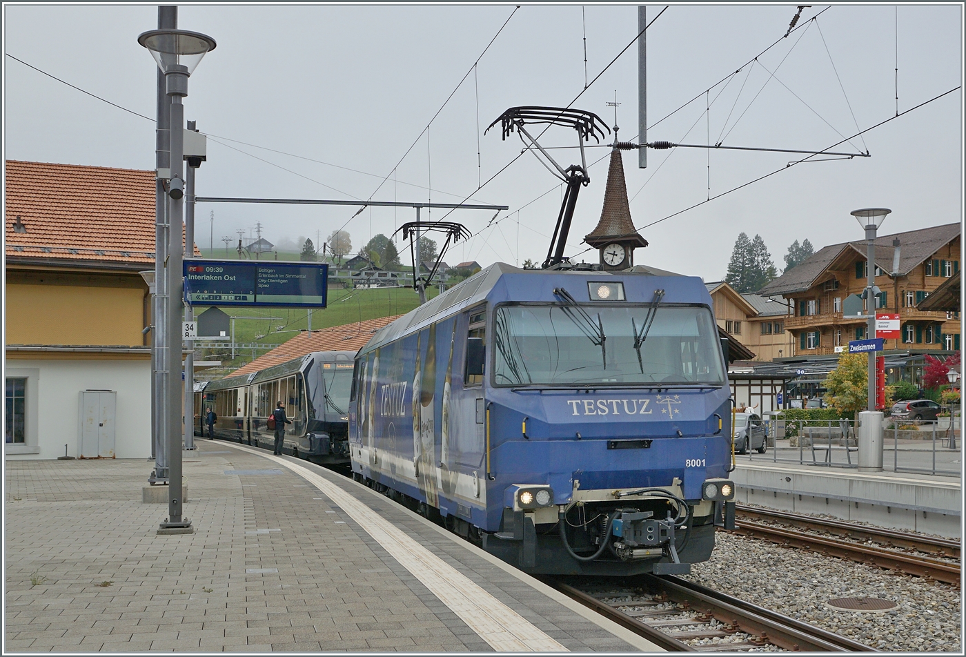 Die MOB Ge 4/4 8001 hat mir ihrem GoldenPass Express PE 4064 von Montreux nach Interlaken Ost den Spurwechselbahnhof Zweisimmen erreicht. Während der Zug bereits umgespurt ist, muss die Ge 4/4 spurwechselbedingt hier ihren Zug verlassen. Am Schluss des Zugs macht sich bereits eine BLS Re 465 (mit einem  Interfacewagen ) bereit um den Zug für die Weiterfahrt nach Interlaken zu übernehmen. 

13. Oktober 2025