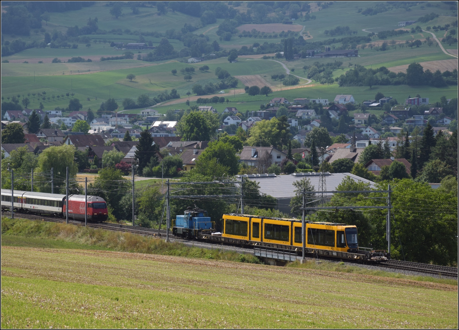 Die Stadler-Werkslok Eem 936 131 liefert eine neue TINA-Strassenbahn nach Darmstadt aus. Auf dem Weg in Frick begegnet der Transport der Re 460 094 'Rhätia' mit einem umgeleiteten IC. Juli 2023.