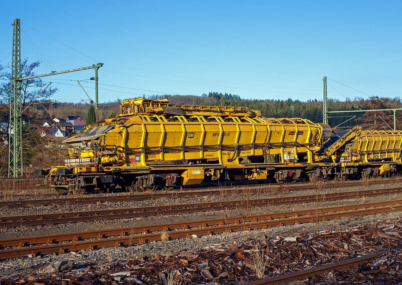 Drei Plasser & Theurer Materialfrder- und Siloeinheiten (MFS 100) der sterreichischen Gleisbaufirme PORR AG (Wien) sind, mit einem Schutzwagen, am 26 Dezember 2024, in Scheuerfeld/Sieg abgestellt.

Hier im Vordergrund die P&T Materialfrder- und Siloeinheit MFS 100 B mit integrierter Beladestation (in Transportstellungen oben auf dem MSF) 99 81 9352 033-0 A-PTU.

TECHNISCHE DATEN:
Hersteller: Plasser & Theurer, Linz an der Donau (sterreich)
Spurweite: 1.435 mm
Lnge ber Puffer: 22.900 mm
Achsanzahl: 8 (in 2 Doppel-Drehgestellen)
Drehzapfenabstand der Doppeldrehgestelle: 15.100 mm
Drehzapfenabstand der Einzeldrehgestelle: 3.900 mm Achsabstand der Einzeldrehgestelle: 1.500 mm
Motorleistung: 165 kW (wassergekhlter Deutz BF6M 1013 C Motor fr Bandantrieb)
Eigengewicht: 67 t
Nutzlast: 77 t ab D4
Fahrgeschwindigkeit in Schleppfahrt leer, max.: 120 km/h
Fahrgeschwindigkeit in Schleppfahrt beladen, max.:100 km/h
Fassungsvermgen: 68 m
Frderleistung (materialabhngig), max.: 700 – 800 m/h
Entladezeit: ca. 5 min
Besonderheit: mit integrierter Beladestation