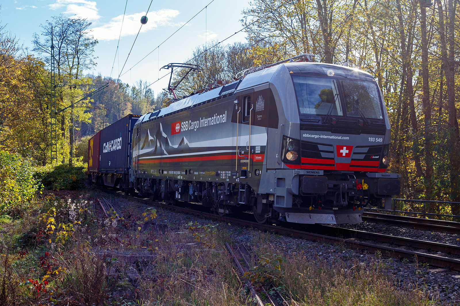 Ein fast fabrikneuer SIEMENS XLoad-Vectron, gerade mal 4 Wochen alt.
Die an die SBB Cargo International AG vermietete 193 539 mit XLoad  Duomo Milano  (91 80 6193 549-3 D-SIEAG) der SüdLeasing GmbH, Stuttgart (eingestellt in Deutschland durch Siemens) fährt am 29.10.2024 mit einem KLV-Zug, durch Kirchen (Sieg) in Richtung Siegen.

Die Multisystemlokomotive Siemens Vectron MS wurde 2024 von Siemens Mobilitiy in München-Allach unter der Fabriknummer 23595 gebaut und am 25.09.2024 ausgeliefert. Sie wurde in der Variante A40-1a ausgeführt und hat so die Zulassung für Deutschland, Österreich, die Schweiz, Italien, die Niederlande und Belgien (D / A / CH / I / NL / B). Sie verfügt über eine Leistung von 6,4 MW (160 km/h) und ist neben den nationalen Zugsicherungssystemen mit dem Europäischen Zugsicherungssystem (ETCS  BL3) ausgestattet. Zudem ist sie mit der neuen Ausrüstungspaket XLoad ausgestattet. 

Das neue XLoad Ausrüstungspaket für Vectron:
XLoad ist ein Ausrüstungspaket für Vectron, welches künftig mitbestellt, aber auch bei bereits ausgelieferten Vectron Loks nachgerüstet werden kann. Das Feature verbessert die Reibwertausnutzung und ermöglicht dadurch höhere Anhängelasten. Zudem reduzieren die Fahreigenschaften, die das Feature bewirken, den Verschleiß von Rad und Schiene.

Aktuell sind die Schweizer Vectron-Lokomotiven (SBB Cargo und BLS Cargo) in der Regel in Doppeltraktion unterwegs. Die Steigungen und Rampen der Schweizer Berge sind vor allem bei schlechten Witterungsbedingungen nicht ohne. Eine Lokomotive muss auch bei geringerem Schlupf genügend Traktion auf die Schienen bringen, um alle Güter sicher und zuverlässig ans Ziel zu bringen. Ein effizienter Weg aus dieser «Misere» ist die für Vectron entwickelte Zusatz-Funktion «XLoad». Den erfolgreichen Beweis trat eine SIEMENS Testlokomotive im Frühjahr 2022 bei der SBB Cargo International und bei der BLS Cargo eindrücklich an. 

Für SBB Cargo International bewies die Test-Lokomotive am Bözberg und für BLS Cargo an der Nordrampe des Lötschbergs ihre enorme Zugkraft. 
Vectron meisterte im Frühjahr 2022 die lange 12‰-Steigung des Bözbergs mit einer Anhängerlast von 2.000 Tonnen bravourös. Bei den nächtlichen Testfahrten zeigte sich eindrücklich die enorme Zugkraft der Lokomotive. 

Am Lötschberg wurden bei der BLS Cargo steigungsmäßig noch ein paar Promille draufgepackt. Mit 1.020 Tonnen im Gepäck bewältigte die Vectron-Lokomotive mit XLoad-Feature die 27‰-Steigung der Nordrampe ebenfalls meisterlich. Und auch diverse Anfahrtsversuche absolvierte der mit dem XLoad-Feature aufgerüstete Vectron problemlos. 

So bestellte die SüdLeasing GmbH (Stuttgart) im Auftrag der SBB Cargo International jüngst 20 Vectron Lokomotiven mit XLoad bei SIEMENS.