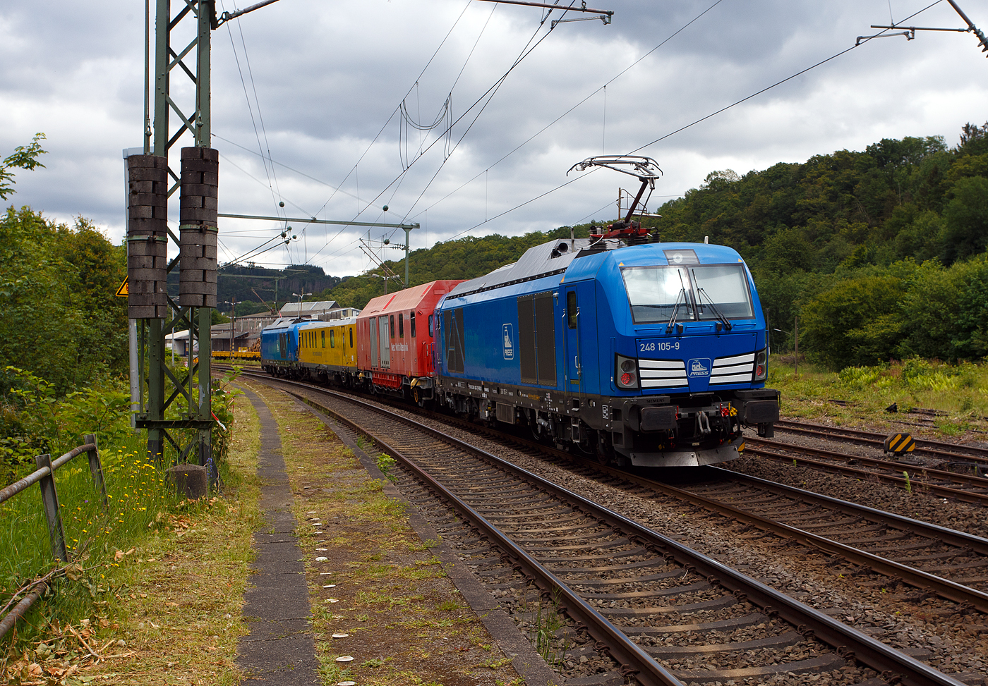 Im Sandwich zweier SIEMENS Vectron Dual Mode fährt ein Schienenprüfzug (SPZ 3), auf Prüffahrt (der Messwagen ist auf die Schiene absenkt) am 14 Juni 2024 durch Scheuerfeld/Sieg in Richtung Siegen.

Die vierteilige Komposition bestand aus:
• Der SIEMENS Vectron Dual Mode der 248 027-5 (90 80 2248 027-5 D-PRESS) alias 248 106-8 der PRESS (Eisenbahnbau- und Betriebsgesellschaft Pressnitztalbahn mbH, Jöhstadt).
• Dem Messwagen SPZ-STW (STW steht für Steuerwagen) 720 301(99 80 9360 006-7 D-DBMP) der DB InfraGO AG, ehemals DB Netz AG (NetzInstandhaltung/Fahrwegmessung).
• Einem Hilfszug-Wagen (Nummer unbekannt) der DB Netz AG (Notfalltechnik) bzw. DB InfraGO AG.
• Und der SIEMENS Vectron Dual Mode der 248 026-7 (90 80 2248 026-7 D-PRESS) alias 248 105-9 der PRESS (Eisenbahnbau- und Betriebsgesellschaft Pressnitztalbahn mbH, Jöhstadt).

Die Energieversorgung vom Messwagen und dem Hilfszug-Wagen erfolgte von den Loks (spartanisch) über außenverlegte Kabel.

Normalerweise ist der Schienenprüfzug ein zweiteiliger Messtriebwagen, bestehend aus Trieb- (ATW - 719 301) und einem Steuerwagen (STW - 720 301), siehe u.a. http://hellertal.startbilder.de/bild/Deutschland~Unternehmen~DB+Netz+AG/773623/der-plasser--theurer-schienenpruefzug-der.html Warum es nun diese Komposition ist, das ist mir nicht bekannt, vielleicht setzt man nun noch mehr auf E-antrieb.

Der Schienenprüfzug wurde 2015 von Plasser & Theurer in Linz (A) unter der Fabriknummer 6003 (SPZ-STW) gebaut. Um Schäden am Oberbau frühzeitig zu erkennen, setzt die Deutsche Bahn AG verschiedene Prüfzüge der Baureihen 719 und 720 ein. Mittels zweier zerstörungsfreier Prüfverfahren werden die Schienen auf Schädigungen untersucht. Bei der Ultraschallprüfung können Materialfehler durch Materialermüdung innerhalb der Schiene bis zum Schienenfuß erkannt werden. Mit der Wirbelstromprüfung wird der Schienenkopf geprüft.

Die beiden SIEMENS Vectron Dual Mode wurden 2022 von SIEMENS in München-Allach, unter den Fabriknummern 23168 und 23169, gebaut und an die PRESS - Eisenbahnbau- und Betriebsgesellschaft Pressnitztalbahn mbH in Jöhstadt geliefert. Die beiden Vectron DM haben die Zulassung in Deutschland für eine Höchstgeschwindigkeit 160 km/h.

Der Vectron Dual Mode vereint die Vorteile einer vollwertigen Diesellokomotive mit denen von elektrischen Lokomotiven. Dank des leistungsstarken Dieselantriebs sowie der Ausstattung für die Nutzung der Fahrleitung kann man jederzeit flexibel auf die Traktionsanforderungen reagieren. So bleibt man immer in Bewegung, egal ob mit oder ohne Fahrdraht. Wo ein Fahrdraht ist, sollte man ihn nutzen. Denn der Betrieb unter Oberleitung ist im Vergleich zum Dieselbetrieb deutlich kosteneffizienter und umweltfreundlicher. Doch weil es in Deutschland noch lange Zeit Strecken geben wird, die nicht vollständig elektrifiziert sind, fahren viele Diesellokomotiven unter Fahrdraht weiter. Das ist aber ökonomisch und ökologisch wenig sinnvoll. Dies ist hier ein Beispiel einer echten Alternative.
