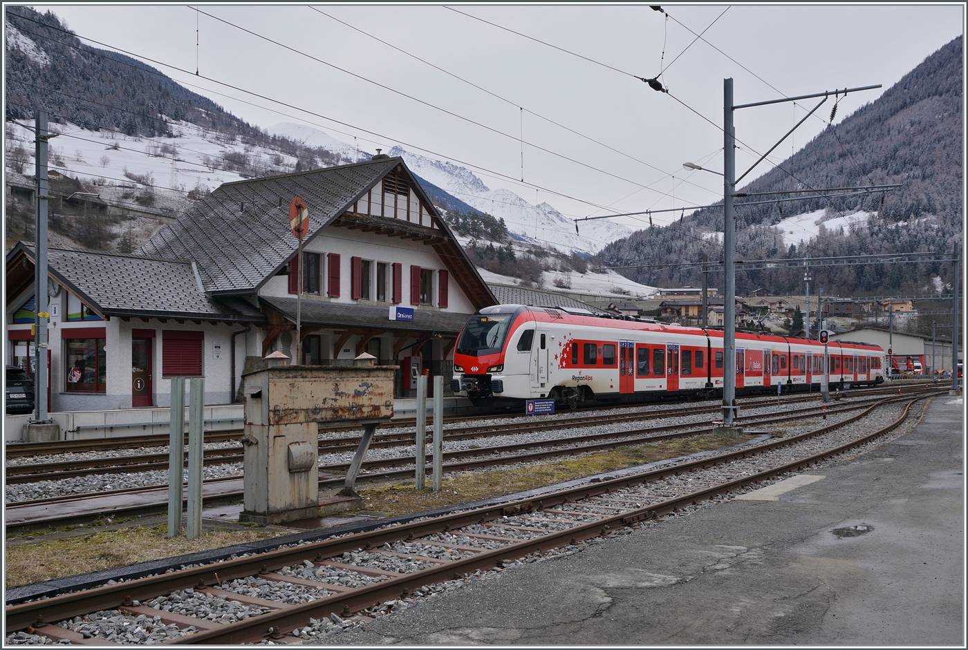 
Im Wallis, in einem versteckten Seitental, schon nahe der Grenze zu Italien, habe ich einen neuen FLIRT gefunden, der auf den Name EVO h�rt. Es wird wohl einer der ersten Z�ge dieser Baureihe im Planverkehr sein: in Orsi�res wartet als herrlicher Kontrast zur Gleiswaage im Vordergrund des Bildes der TMR Region Alpes RABe 533 601 (UIC Nummer RABe 94 85 0 533 701-4 CH-RA) mit dem Wappen  Commune de St L�onard  und dem dazu passenden Namen  La Souterraine  als R82 26325 auf die Abfahrt nach Sembrancher. 24. Januar 2026