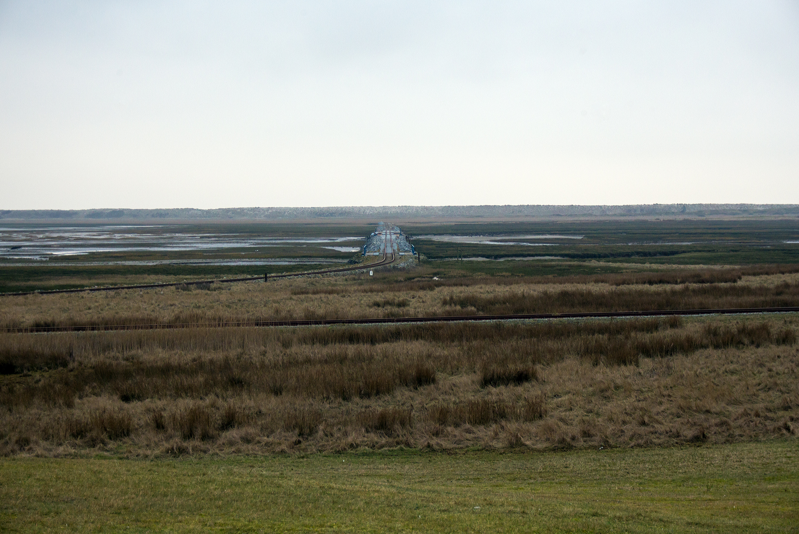 Inselbahn Wangerooge beim Abzweig Wangerooge Saline (vom Deich gesehen) am 12 März 2024. 

Geradeaus in der Bildmitte die Strecke auf dem Steindamm in den Salzwiesen zum Westanleger Wangerooge, mit einer Länge von rund vier Kilometern verbindet die Inselbahn den Ort Wangerooge mit dem Westanleger. Hier auf halber Strecke führt das Gleis über einen Priel. Mehrere Eisenbahnbrücken ermöglichen den Tidefluss (auf- und abfließen Gezeiten) im Priel zwischen der Salinenbucht und der Westlagune. 

Vorne (von links nach rechts) die Stichbahn/Strecke Wangerooge Saline zu Wangerooge Westen. 

Die Inselbahn Wangerooge ist die einzige von der Deutschen Bahn betriebene Schmalspurbahn und das wichtigste Verkehrsmittel auf der autofreien Insel. Sie ist auch eine der letzten Schmalspurbahnen Deutschlands mit Güterverkehr. Sie ist die einzige deutsche Inselbahn mit einer Zweigstrecke.
