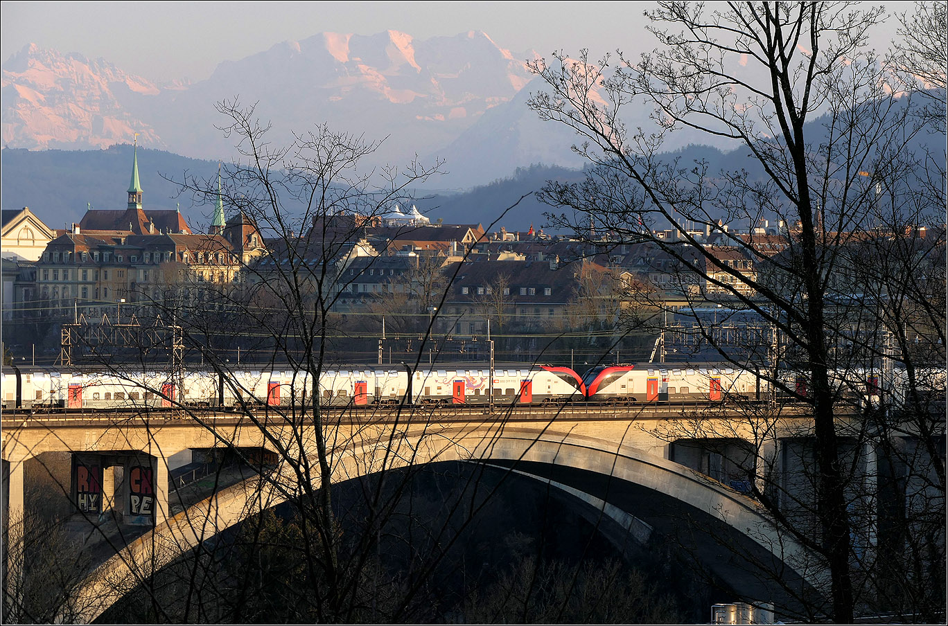 Mit Peter unterwegs in Bern - 

Bei schon tief stehender Abendsonne fährt eine RABe 502 Doppeltraktion über den Lorraineviadukt kurz vor dem Hauptbahnhof Bern.

Die Berggipfel: Ganz links das Gspaltenhorn, in Bildmitte zusammenhängend der Morgenstern, Wyssi Frau und Blüemlisalphorn, dann hinter dem Zweig der Niesen und hinter dem Baumstamm das Doldenhorn.

07.03.2025 (M)