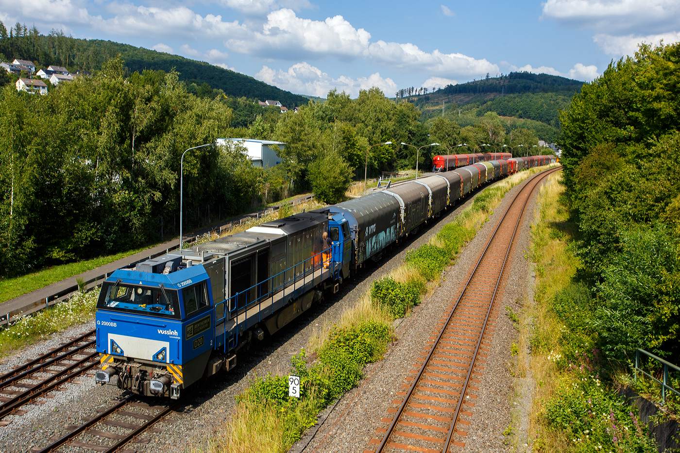 Nun hat der ganze lange Coilzug den KSW-Rangierbahnhof (Betriebsstätte FGE - Freien Grunder Eisenbahn) in Herdorf am 25 Juli 2025 erreicht. Hier am Zugschluss die nachschiebende an die KSW vermietete 272 408-6 / D20 der Bentheimer Eisenbahn AG (92 80 1272 408-6 D-BE), ex Rurtalbahn V 203 (92 80 1272 408-6 D-RTBC), eine Vossloh G 2000BB (mit symmetrischem Führerhaus). Vorne (ganz hinten rechts im Bild) die KSW 44 (92 80 1271 004-4 D-KSW) eine MaK G 1000 BB. Rechts die DB-Strecke KBS 462 „Hellertalbahn“.

Für die Talbahn (Freien Grunder Eisenbahn) zum Pfannenberg ist der Zug einfach zu lang, so wird er hier geteilt und die KSW 44 zieht später 9 oder 10 Wagen weiter zum Pfannenberg. Wobei für die Spitzkehre Pfannenberg ist dann dieser Zug auch nach zu lang und er wird in Neunkirchen-Salchendorf nochmals geteilt. 