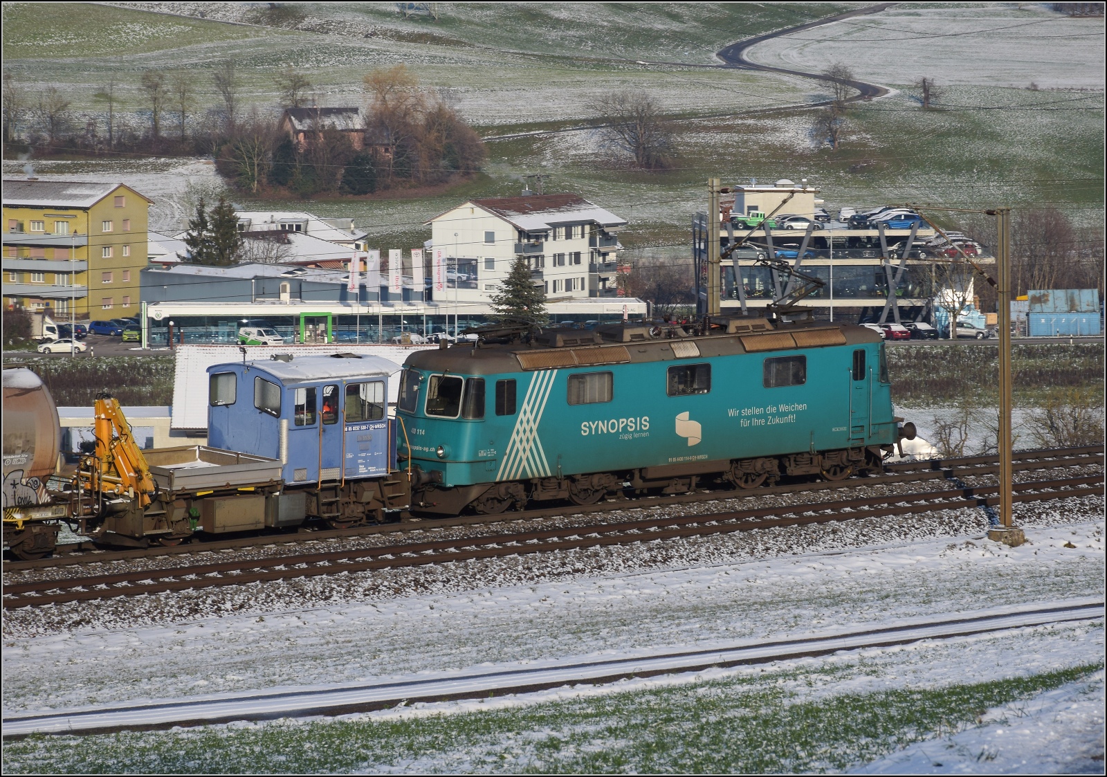 Re 430 114 von WRS mit Synopsis-Werbung schleppt die Rangierhilfe Tm III 9530 mit über den Bözberg. Frick, Dezember 2022.
