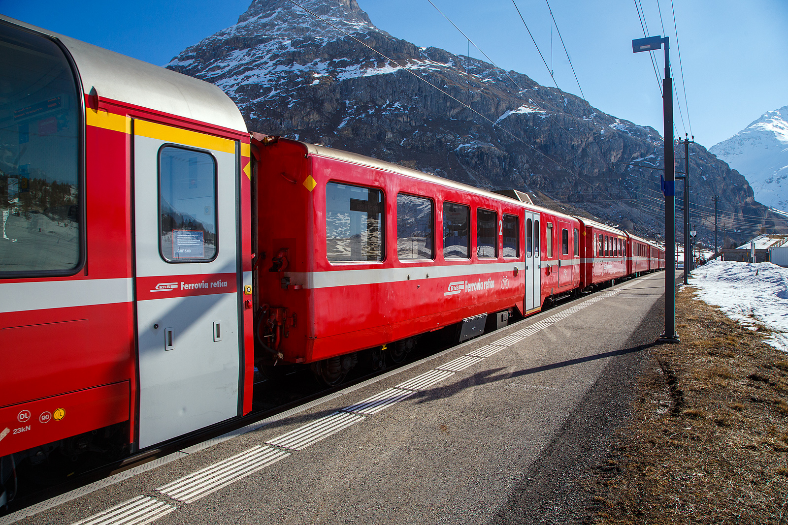 RhB Berninabahn Velowagen, ein verkrzter 2.Klasse Mitteleinstiegswagen mit Gepckabteil in leichter StahlbauartRhB WS 3931, ex RhB BD 2477, ex RhB B 2334, ex B4 2334, am 22.03.2023 in der Station Bernina Diavolezza (2.082 m . M.) im Zugverbund. Wegen der Steckengeometrie, mit Radien von teils nur 50 m, mssen auf der Berninalinie krzer Wagen, als auf dem Stammnetz, eingesetzt werden.

Am 13.09.2017 konnte ich ihn noch als BD 2477 in Ospizio Bernina ablichten, siehe http://hellertal.startbilder.de/bild/schweiz~wagen~personenwagen-rhb-schmalspur/644168/rhb-bd-2477-ein-verkuerzter-2klasse.html

1956 bis 1957, kurz nach Abschaffung der dritten Klasse, erhielt die RhB noch einmal 13 Leichtstahlwagen. Diesmal kamen die Wagen von SIG Neuhausen und wiesen aber viele Gemeinsamkeiten mit den Leichtmetallwagen frherer Bauart auf: Flgeltren, WC beim Mitteleinstieg, Stirnwandtren direkt im Personenabteil, gleicher Sitzteiler. Die Wagen waren aber 18.26 m lang, liefen auf SIG-Torsionsstab-Drehgestellen (System Frei). Die Wagen erfuhren verschiedene Umbauten zu Steuerwagen (BDt 1731), Pendelzugwagen, Velowagen und verkrzten Wagen (BD 2477–2478) fr die Berninalinie. Dabei erhielten sie auen bndige Schwenktren.

Dieser Wagen wurde 1956 gebaut als B4 2334 geliefert, spter in B 2334 umgezeichnet. Im Jahr 2003 fr den Einsatz auf der Berninabahn verkrzt und zum 2.Klasse Wagen mit Gepckabteil umgebaut, 2019 erfolgte ein weitere Umbau zum heutigen Velowagen WS 3931, wobei wie hier im Winter dient er als Skiwagen.

TECHNISCHE DATEN:
Baujahr und Hersteller: 1956 - SIG
Spurweite: 1.000 mm
Anzahl der Achsen: 4
Lnge ber Puffer: 16.220 mm
Drehgestellart: SIG Torsionsstab
Sitzpltze: 30
Eigengewicht: 19,0 t
Ladeflche: 9 m
Ladegewicht: 2,0 t
Max. Gesamtgewicht: 25 t
zulssige Geschwindigkeit: 90 km/h
Lauffhig: StN (Stammnetz) / BB (Berniabahn) / MGB (Matterhorn Gotthard Bahn)
