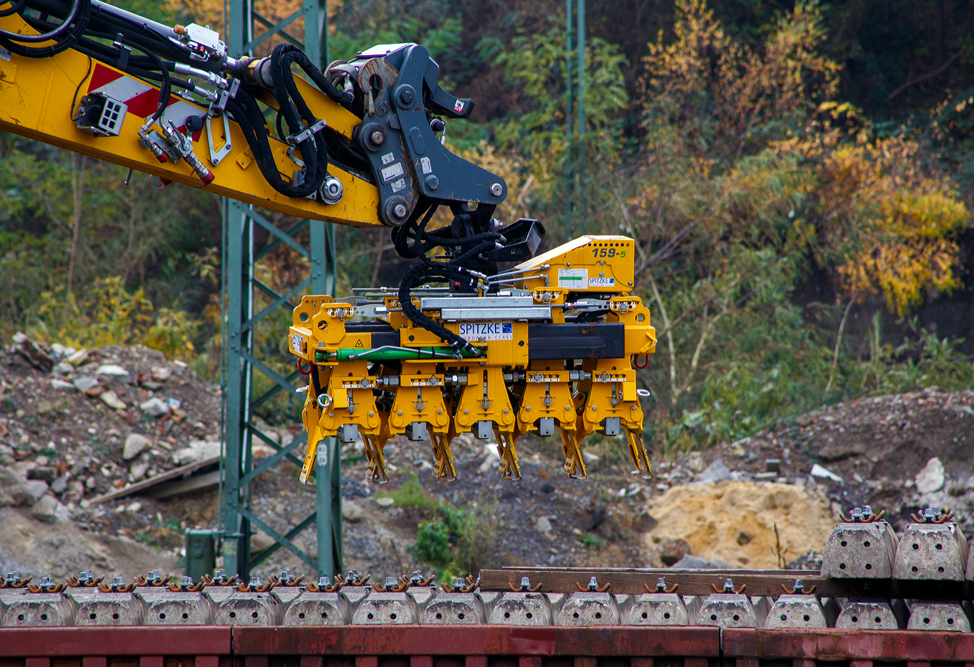 Schwellenverlegegerät Typ 159-5 (Hersteller Sonnenberg GmbH) am 08 November 2025 an einem LIEBHERR Zweiwegebagger A 922 Rail Litronic der SPITZKE SE (Großbeeren) im Rbf Betzdorf/Sieg. Hier werden zurzeit Gleise erneuert.

Der Schwellenleger ist eine innovative Neuentwicklung in Sachen Verlegetechnik. Durch das mittige Aufnehmen der Schwellen ist ein Anlegen an eine Lehrschiene möglich, wodurch kein Ausrichten der Schwellen mehr erforderlich ist.

•	Einfache Einstellung des Schwellen Typs und des Verlegeabstandes durch ein Bolzensystem.
•	Schwellentyp: Grobeinstellung der Schwellenbreite und Höhe in 10 mm Schritten. Feineinstellung der Schwellenbreite über ein Gewinde möglich.
•	Verlegeabstand: Grobeinstellung in 18 x 5 mm Schritten, Feineinstellung und größere Maß-Sprünge über ein Gewinde.
•	Die Greifer sind aus hochfestem und verschleißbeständigem Stahl (Hardox) gefertigt. Für einen besonders schonenden Umgang mit den Schwellen sind sie mit einem Hochleistungskunststoff ausgestattet.
•	Wartungsfreie und selbstschmierende Gleitkörper und Buchsen reduzieren den Wartungsaufwand auf ein Minimum.
•	Die Greiferzylinder sind mit Lasthalteventilen ausgerüstet um maximale Sicherheit zu gewährleisten.

TECHNISCHE DATEN:
Traglast: 3.300 kg
min. Schwellenbreite: 280 mm
max. Verlegeabstand: 750 mm
Gewicht Variante 159–5 für 5 Schwellen:  ca. 700 kg
Kleinste Transportabmessung (Variante 159–5): 1550 x 1000 mm
