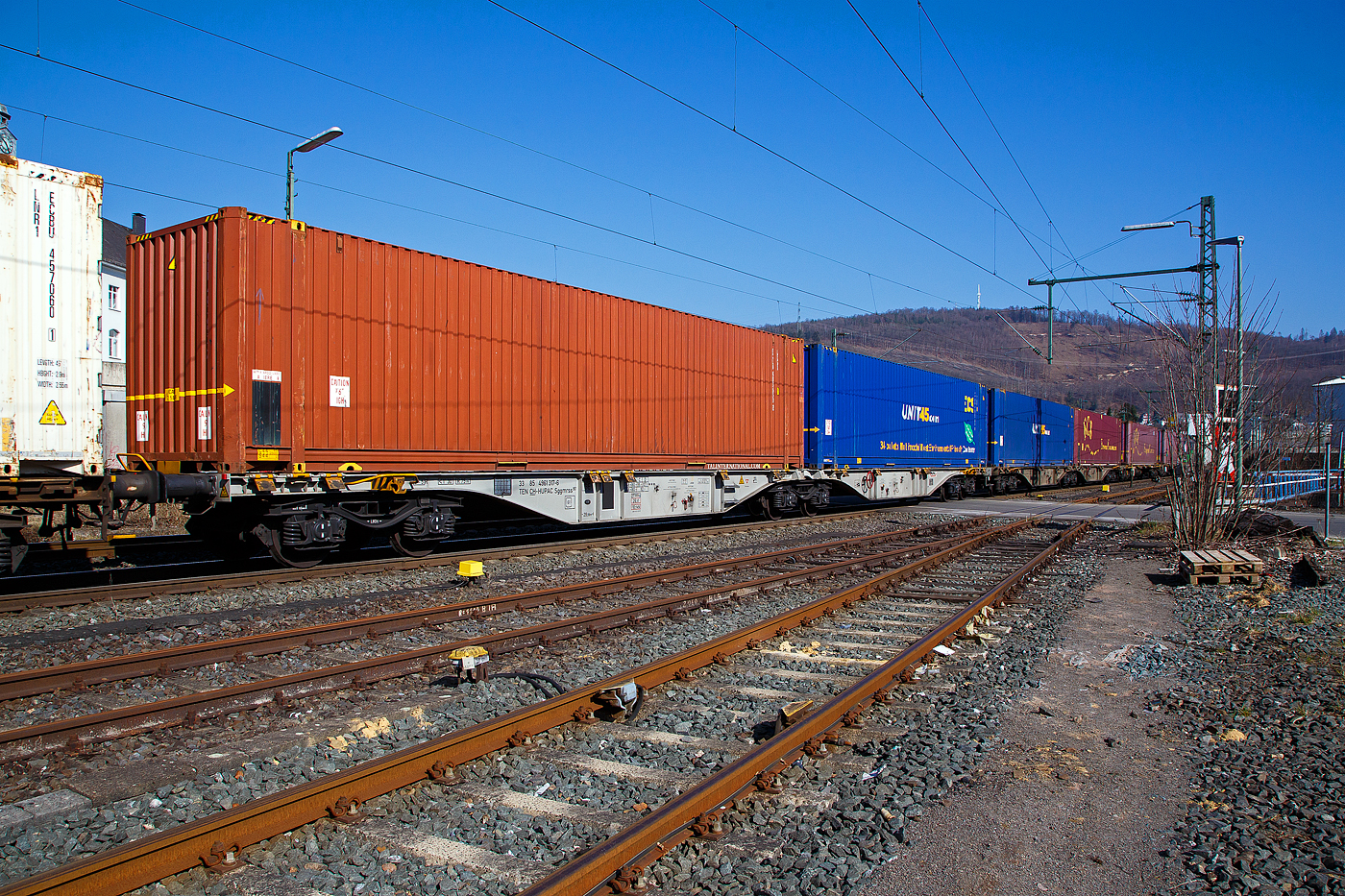 Sechsachsiger Drehgestell-Gelenk-Containertragwageneinheit 90´, 33 85 4961 317-6 CH-HUPAC der Gattung Sggmrss 90`der HUPAC AG am 24.03.2021 im Zugverband bei der Durchfahrt in Niederschelden an der Siegstrecke (KBS 460) in Richtung Siegen.

Diese Gelenkwagen mit sechs Radsätzen sind für den Transport von Großcontainern und Wechselbehältern vorgesehen. Auf den Außenlangträger des Wagens befinden sich für jede vorgesehene Ladeposition feste und klappbare Aufsetzzapfen zum Festlegen der Ladungseinheiten (gemäß UIC- Merkblatt 592-1 und 2) in verschiedenen Kombinationen.

Das aus zwei Wagenhälften bestehende Untergestell ist eine verwindungsweiche, geschweißte Rahmenkonstruktion aus Walz- und Blechprofilen, gebildet aus den Kopfstücken, den Hauptquerträgern und den äußeren Langträgern. In der Wagenmitte befindet sich eine Übersteigmöglichkeit.

TECHNISCHE DATEN:
Spurweite: 1.435 mm
Länge über Puffer: 29.590 mm
Drehzapfenabstand: 2 x 11.995 mm
Achsabstand in den Drehgestellen: 1.800 mm
Drehgestelle: 3 x Y25Lss1-K
Laufraddurchmesser: 920 mm (neu)
Ladelänge: 2 x 13.820 mm
Höhe der Ladeebene über S.O.: 1.155 mm
Eigengewicht: 27.300 kg
Max. Zuladung bei Lastgrenze S: 107,7 t (ab Streckenklasse D)
Max. Zuladung bei Lastgrenze SS: 92,7 t (ab Streckenklasse C)
Max. Geschwindigkeit: 100 km/h (Lastgrenze SS und leer 120 km/h)
Kleinster befahrbarer Gleisbogen: R 75 m 
Bremse: 2 x KE-GP-A 
Bremssohle: Jurid 816M
Feststellbremse: Ja
Verwendungsfähigkeit: TEN GE
