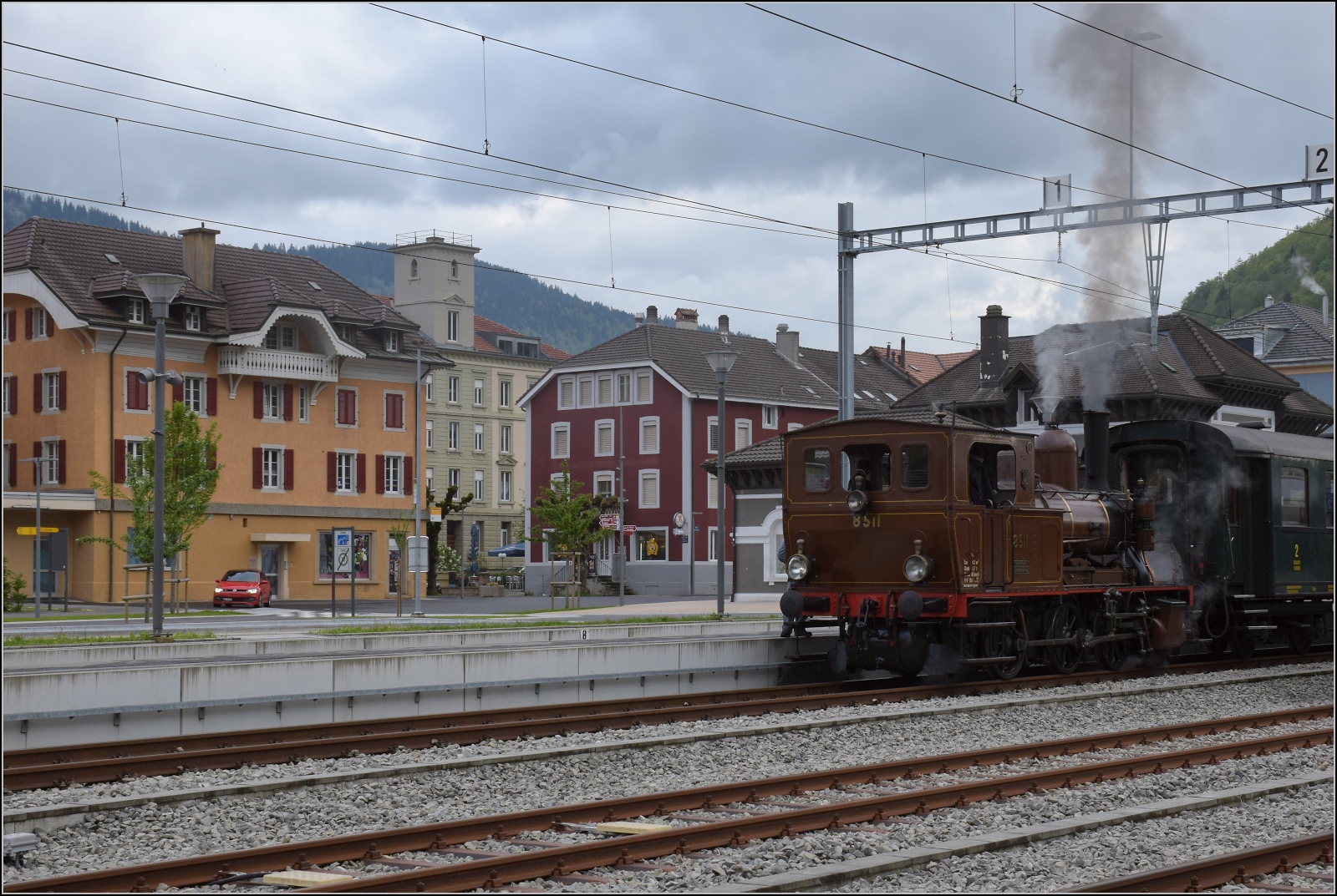 Vapeur Val-de-Travers: Train du Terroir.

Mit Blick in den Ort Fleurier wartet E 3/3 8511 auf den Gegenzug. Mai 2023.
