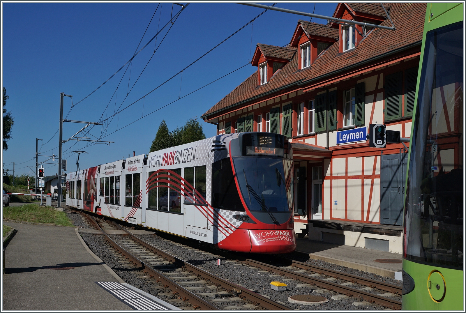 Vor dem hübschen Gebäude des Bahnhof von Leymen kreuzen sich sind BLT Züge nach Rodersdorf (nur schwach angeschitten) und Dornach.

26. Sept. 2023