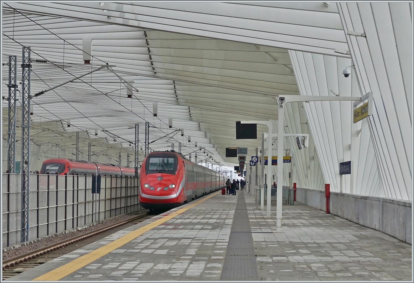 Während ein FS Trenitalia ETR 500 in der wunderschönen Halle des Bahnhofs von Reggio Emilia AV auf der Fahrt nach Norden kurz anhält; fährt kaum zu sehen links im Bild der bereits bei der Einfahrt gezeigte ETR 400 044 mit einem sehr hohen Tempo durch den Bahnhof. 
Der Bahnhof wurde durch den Architekten Santiago Calatrava geplant.

14. März 2023