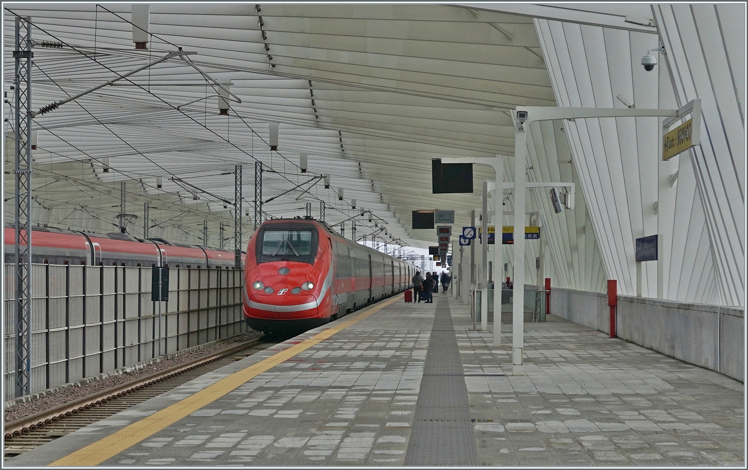Während ein FS Trenitalia ETR 500 in der wunderschönen Halle des Bahnhofs von Reggio Emilia AV auf der Fahrt nach Norden kurz anhält; fährt kaum zu sehen links im Bild ein ETR 400 mit einem sehr hohen Tempo durch den Bahnhof. Der Bahnhof wurde durch den Architekten Santiago Calatrava geplant. 14.03.2023