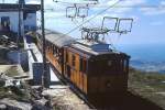 In der Bergstation steht eine der von SLM gebauten Zahnradlokomotiven der Chemin de Fer de La Rhune im April 1986 abfahrbereit mit einem Zug hinunter zum Col de Saint Ignace. Genau über den Gipfel des La Rhune verläuft die französich-spanische Grenze. An klaren Tagen reicht der Blick von den schneebedeckten Gipfeln der Pyrenäen im Osten bis weit auf den im Westen gelegenen Atlantik.