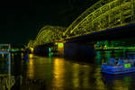Blick auf die Hohenzollernbrücke in Köln am Abend (20:13 Uhr) des 18 Oktober 2014. Blickrichtung vom linken Rheinufer Rheinaufwärts, auf der anderen Rheinseite liegt Deutz. Mit etwa 1220 Zugfahrten pro Tag ist sie eine der meistbefahrenen Eisenbahnbrücken in Deutschland, nur an diesem Tag sah man bedingt durch einen Streik der GDL kaum einen Zug auf der Brücke.

Die Hohenzollernbrücke wurde von 1907 bis 1911 gebaut. Sie ersetzte die Dombrücke, die den Anforderungen des stetig zunehmenden Eisenbahnverkehrs nicht länger gewachsen war. Das Besondere am Bau der neuen Brücke war, dass sie unter laufendem Betrieb der Dombrücke errichtet wurde und diese nach und nach ersetzte. Sie bestand nach ihrer Fertigstellung aus drei nebeneinander liegenden Fachwerkbogenbrücken mit jeweils drei Bögen.

Die Hohenzollernbrücke ist die einzige Brücke in Köln, die nicht durch Bomben zerstört wurde. Vielmehr übernahm es die Wehrmacht am 6. März 1945 selbst, den herannahenden Alliierten durch Sprengung der Brücke eine Rheinüberquerung zu erschweren. Nach dem Krieg wurde bis 1948 zunächst eine der (zweigleisigen) Bahnbrücken wieder aufgebaut. Die Straßenbrücke wurde aus verkehrstechnischen Gründen nicht wiederhergestellt. In den Jahren 1956 bis 1959 und von 1986 bis 1987 wurde jeweils ein weiterer Fachwerkbogen hinzugefügt, so dass die Bahn heute über sechs Gleise auf der Hohenzollernbrücke verfügt. Die zwei nördlichen Gleise sind der S-Bahn vorbehalten. Bei der Hohenzollernbrücke gibt es zu beiden Seiten Geh- und Radwege, die von der Stadt Köln unterhalten und gepflegt werden, während sich die Brücke selbst, wie auch die Südbrücke, im Eigentum der Deutschen Bahn AG befindet.

Mit etwa 1220 Zugfahrten pro Tag ist sie eine der meistbefahrenen Eisenbahnbrücken in Deutschland.  Das Bauwerk gilt, zusammen mit dem Kölner Hauptbahnhof, als zentraler Engpass im Schienenverkehr in der Region Köln.

Technische Daten:
Typ: sechsgleisige Eisenbahnbrücke mit Geh- und Radwegen auf beiden Seiten
Bauart: drei nebeneinander liegende Fachwerkbögenbrücken
Baujahre: je eine Brücke 1946 bis 1948, 1956 bis 1959 und 1986 bis 1987
Spannweiten: 111,88 Meter - 167,75 Meter - 122,56 Meter, insgesamt 409,19 Meter
Gesamtbreite: 26,20 Meter
