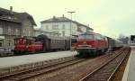 215 005-0 wartet um 1980 vor einem Eilzug nach Ulm im Bahnhof Friedrichshafen Stadt auf Fahrgäste, der Dampf zwischen Lok und Packwagen zeigt, dass die Dampfheizung in Betrieb ist.