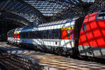 Licht und Schatten unter der bzw. durch Bahnsteigberdachung vom Hbf Kln....
SBB 1.Klasse Reisezugwagen (EC-Wagen) Apm 61 85 10-90 255-3 CH-SBB am 12.08.2022 im Hbf Kln eingereiht in einen EC.

Die EuroCity-Wagen (Apm EC und Bpm EC) der SBB sind zwar nach hnlichen Prinzipien aufgebaut worden, werden aber in der Schweiz nicht als Einheitswagen bezeichnet. Konstruktiv zur gleichen Gruppe gehren die Bt IC, die mit den EW IV eingesetzt werden und lediglich eine Einspannungsausrstung (fr 1000 V, 16,7 Hz) aufweisen. 1989–1995 stellten die SBB eine weitere Groraumwagen Serie fr den EuroCity-Verkehr in den Dienst, die auf den 1980 abgelieferten Bpm RIC und dem EW IV aufbaute. Fr beide Wagenklassen wurde der gleiche Wagenkasten mit zehn Fenstern zwischen den Schwenkschiebetren an den Wagenenden benutzt. Das Dach war von der gleichen Bauart wie beim franzsischen Corailwagen, die Lngssicken waren aber schon bei den Einheitswagen I bis IV vorhanden. Die Schrzen wurden tiefer gezogen als beim EW IV, so wie es fr den EW V vorgesehen war. In den Abmessungen entsprechen die Wagen dem UIC-Z1-Standard. Die Farbgebung in zwei Grautnen mit hellem Streifen dazwischen wurde zuvor bereits fr die zu zweiklassigen EuroCity-Zgen umgebauten TEE-Zge (RABe) angewendet. Der helle Streifen des Eurofima-Anstrichschemas wurde beibehalten. Der Bereich ber dem weien Begleitstreifen war nun in Umbragrau gehalten, darunter im helleren Verkehrsgrau A (RAL 7042). Die 60 Sitzpltze der ersten und 78 der zweiten Klasse sind durchgehend in Vis--vis-Anordnung gehalten. Diese Wagen sind voll RIC-fhig und fr eine Hchstgeschwindigkeit von 200 km/h zugelassen. Insgesamt wurden 70 Apm und 155 Bpm geliefert.

TECHNISCHE DATEN:
Spurweite: 1.435 mm
Anzahl der Achsen: 4 in 2 Drehgestellen
Lnge ber Puffer: 26.400 mm
Drehzapfenabstand: 19.000 mm
Eigengewicht: 45 t
Hchstgeschwindigkeit: 200 km/h
Sitzpltze: 60 (in der 1. Klasse)
Toiletten: 1
Bremse: O-PR-Mg