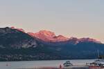 Blick vom Schiffsanleger bei Annecy, auf die noch von der Sonne beschienen Berge am Lac d’Annecy.